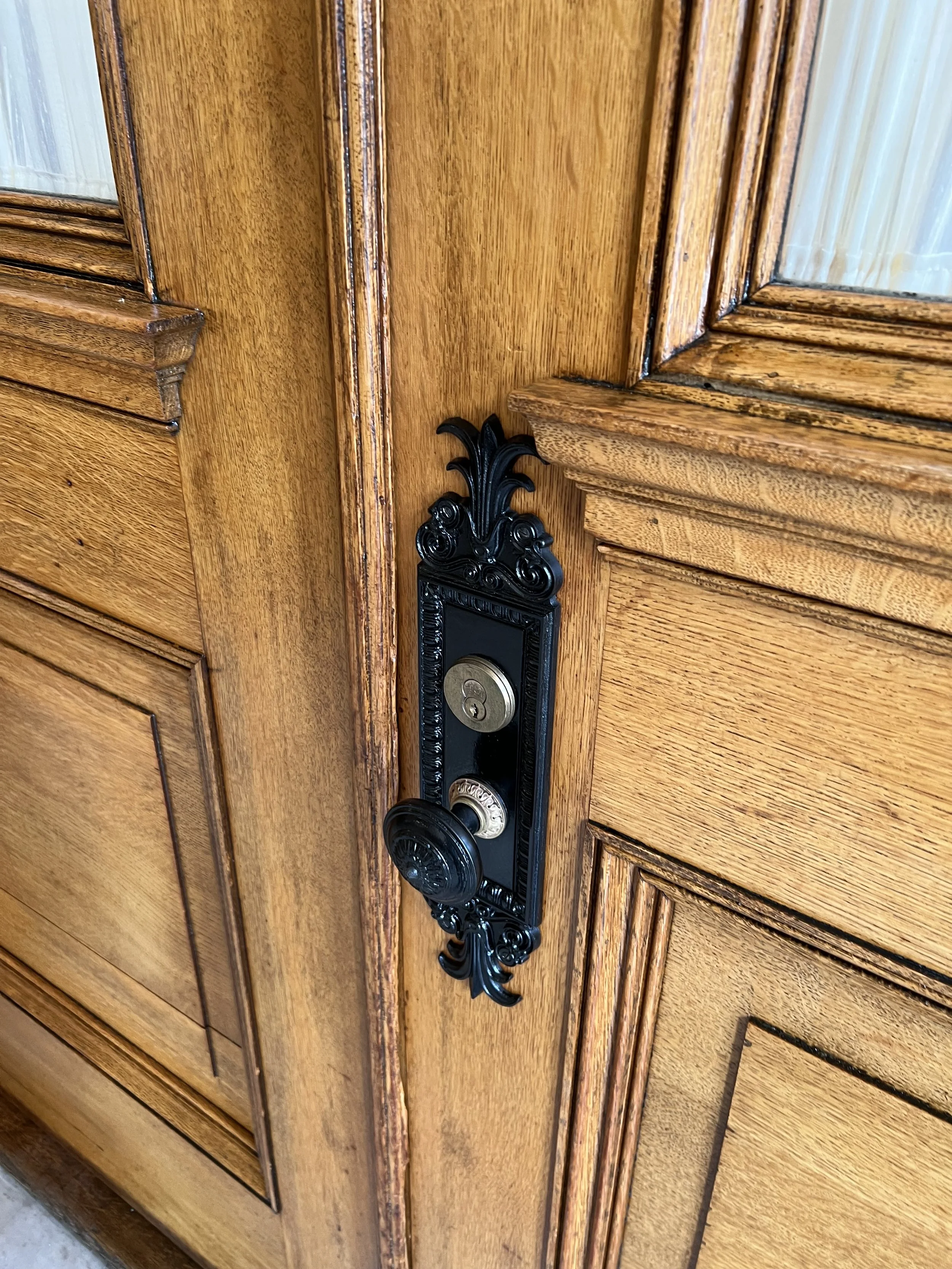 A wooden door with a black ornate door handle and lock.
