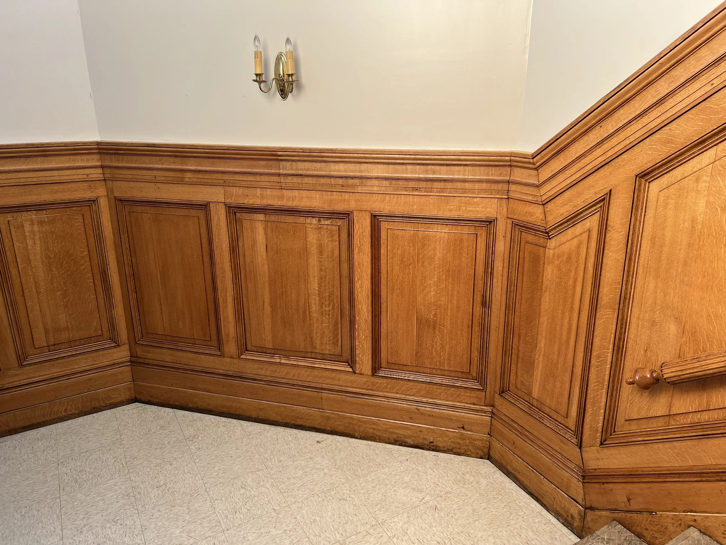 Wooden wainscoting panels with crown molding and a brass wall sconce with two tapers