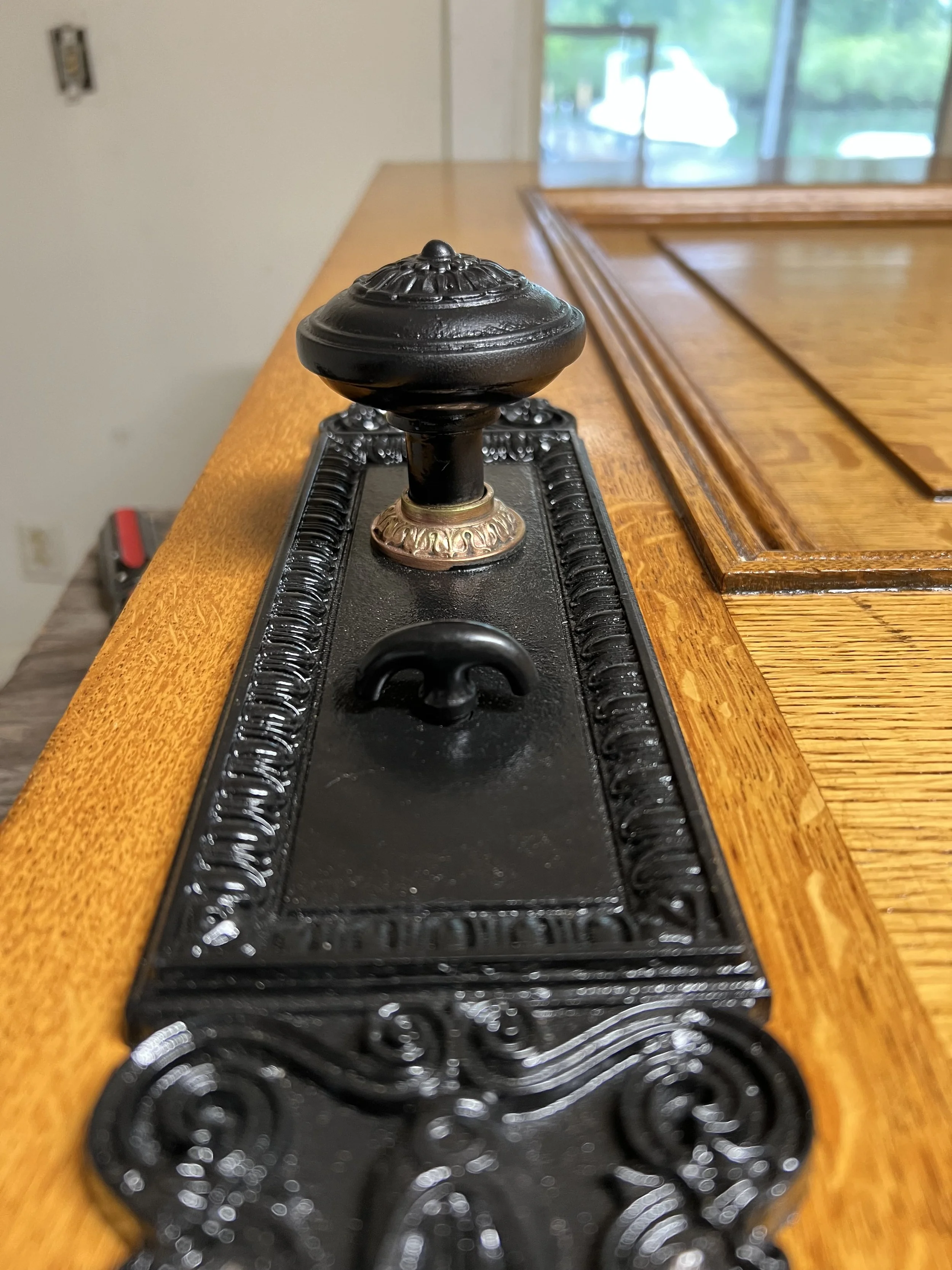 Close-up of a black decorative finial on a wooden furniture piece with a tray underneath, in a room with a window and outdoor scenery in the background.