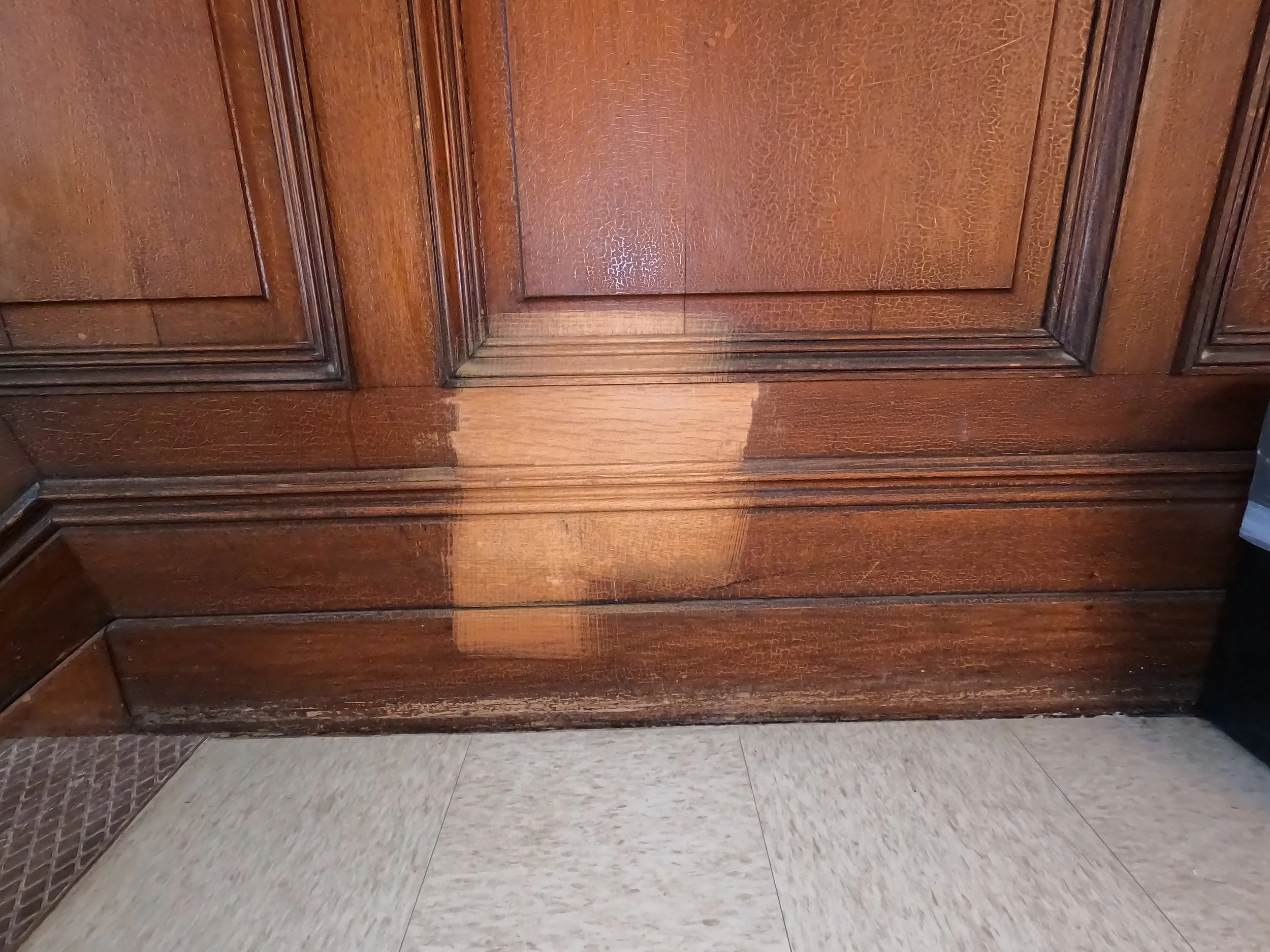 Wooden door panel with detailed molding, Test spot completed with our stripping technique , with a tiled floor at the base.