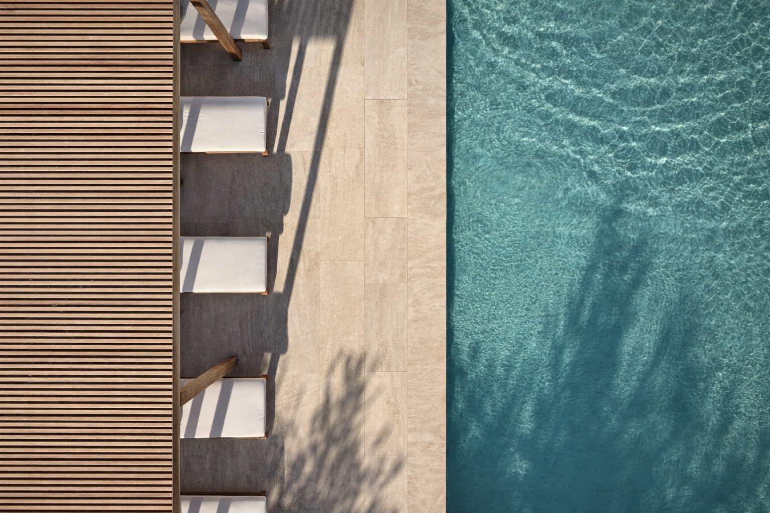 Top-down view of a poolside area with wooden slats, white chairs, and clear blue water.