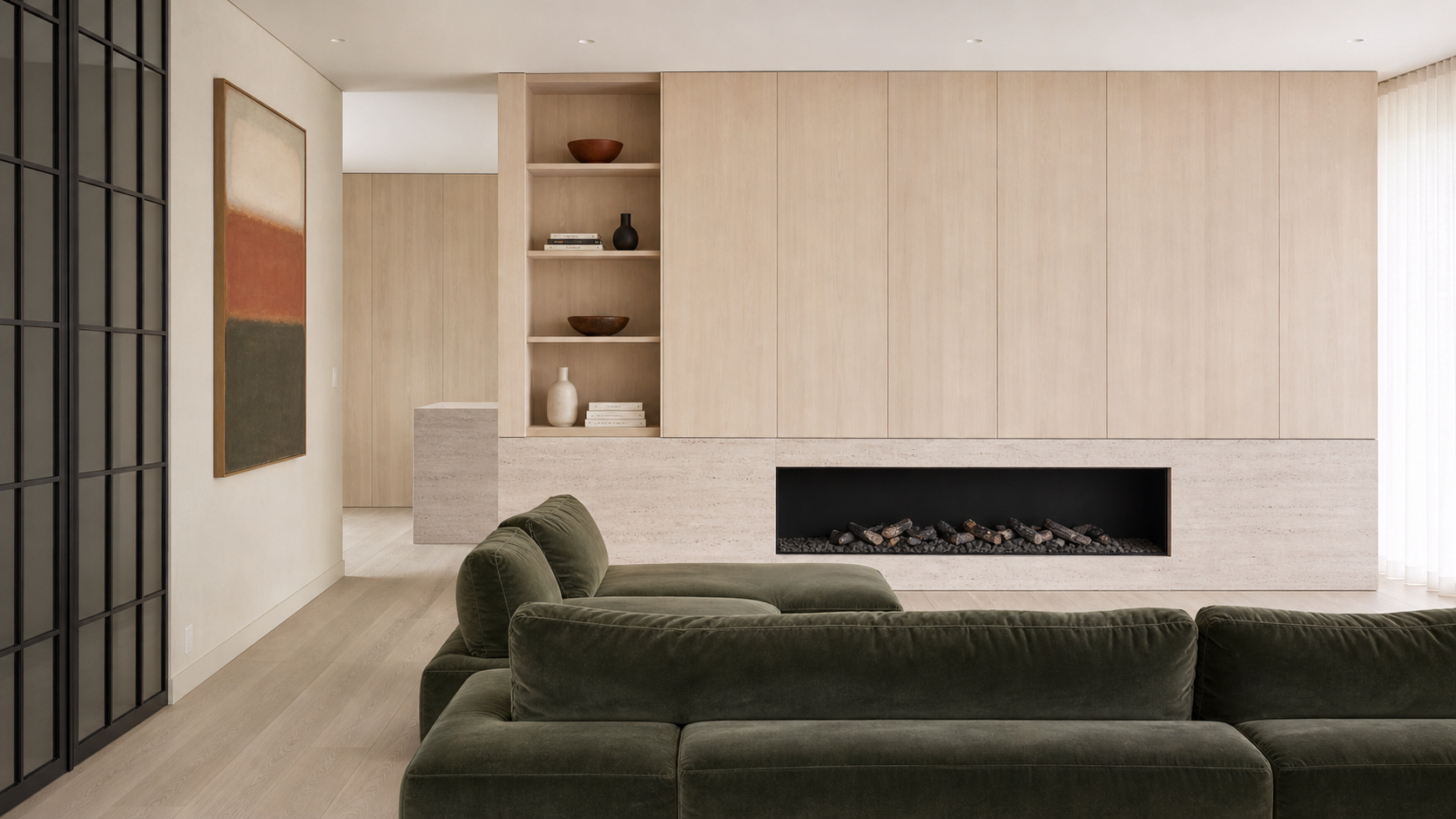 Modern living room with a green velvet sofa, built-in beige wood storage with decorative vases and bowls, in front of a fireplace with stacked firewood, and a large abstract painting on the wall.