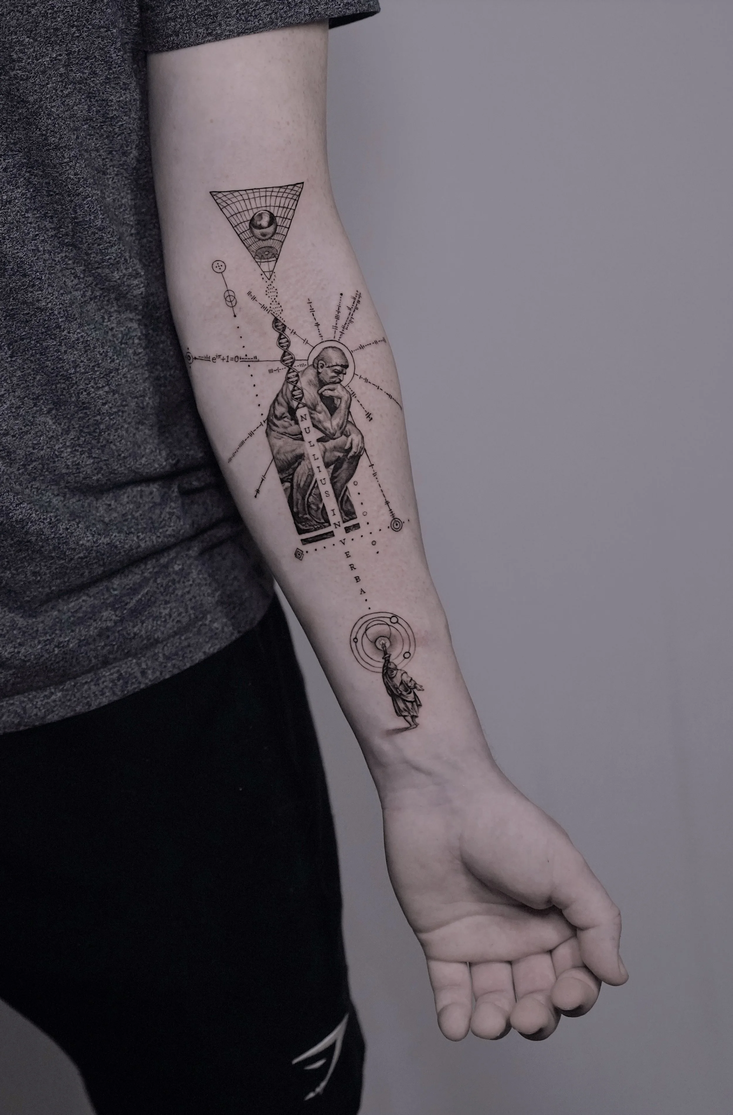 Tattoo on person's forearm featuring a thoughtful man sitting with DNA strands, mathematical symbols, geometric shapes, and the words "nullius in verba".
