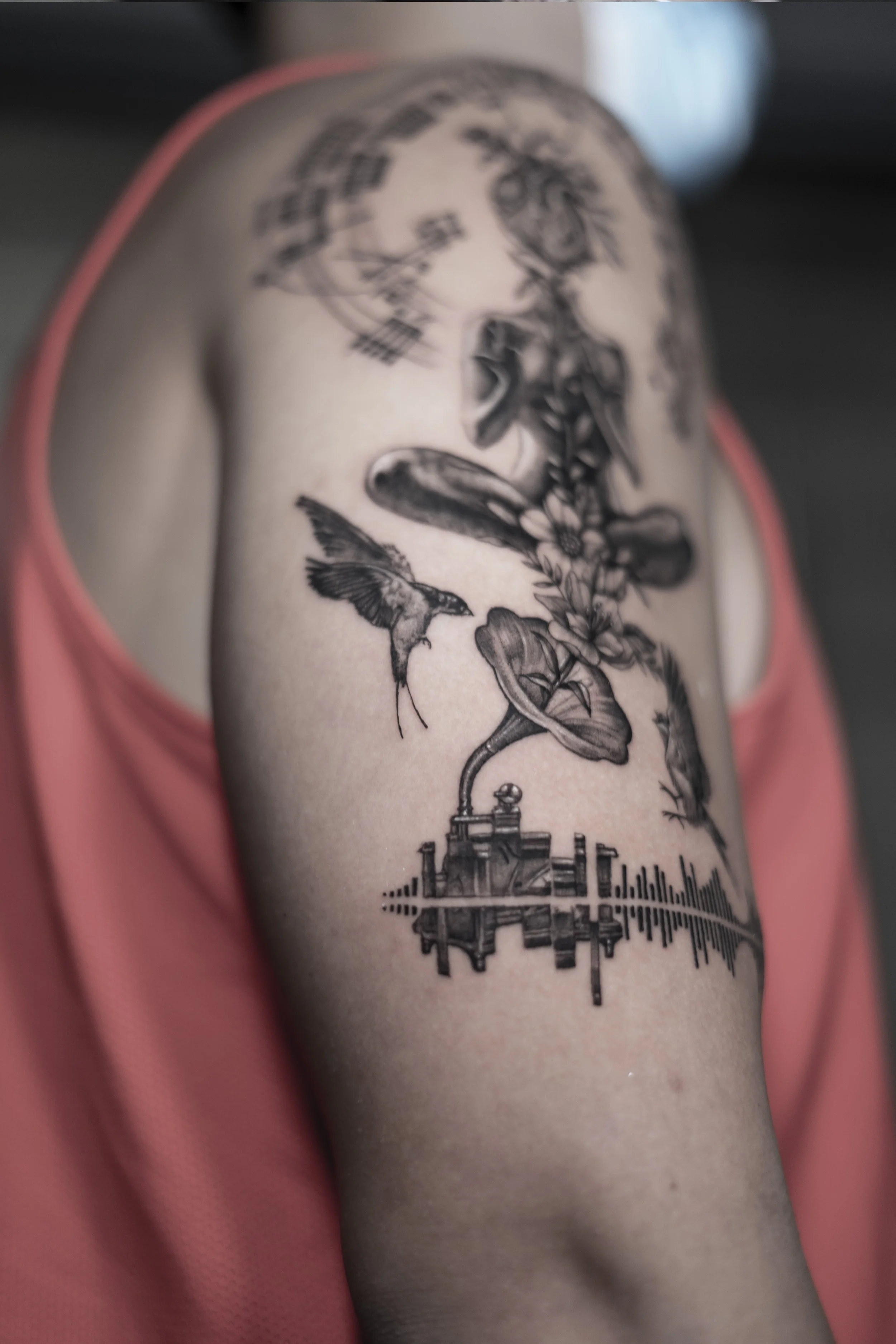 Tattoo sleeve featuring a hummingbird, floral elements, an old-fashioned train, and sound wave patterns on a person's upper arm.