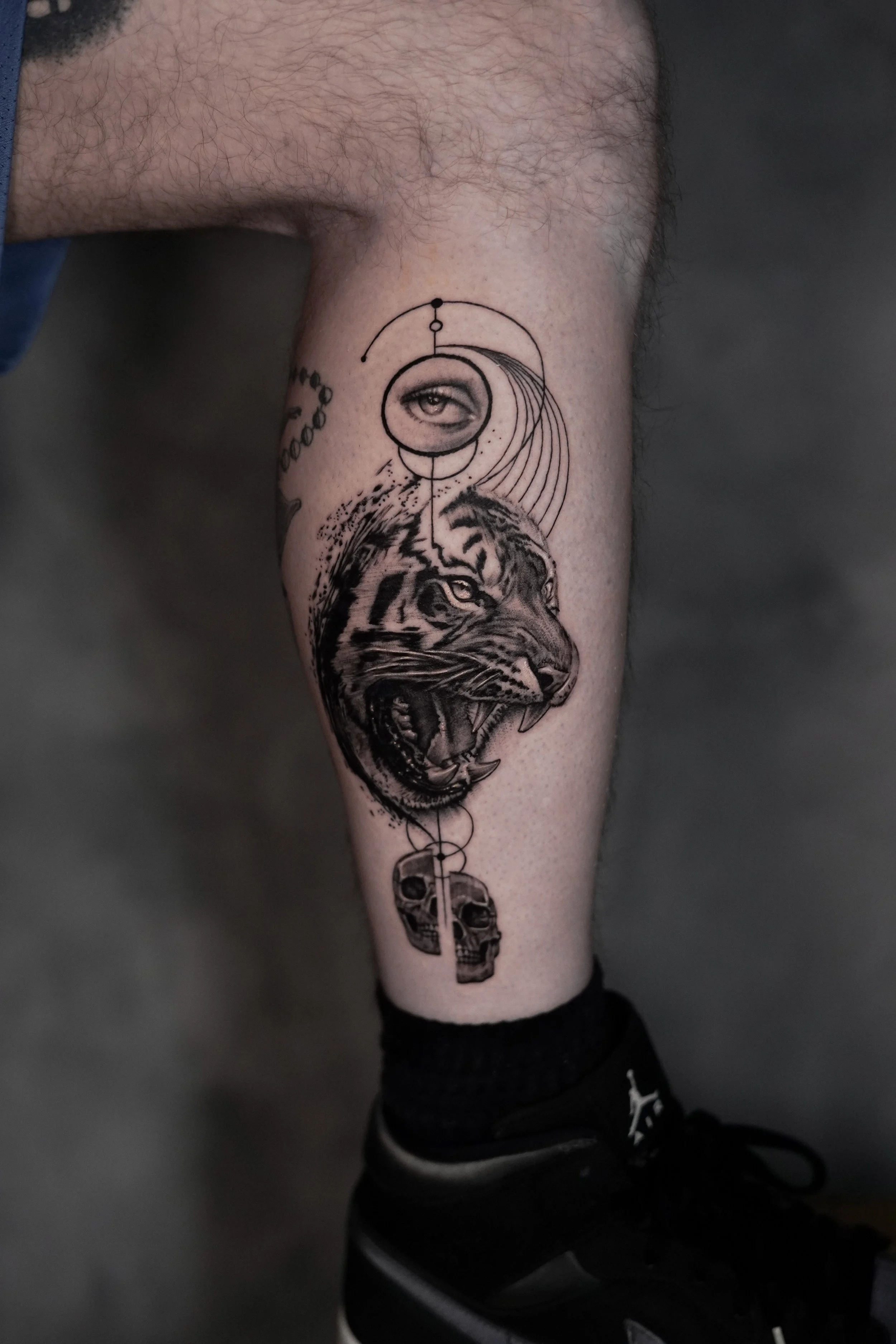 Tattoo of a tiger's head, a human eye, planets, and a skull on a person's calf.