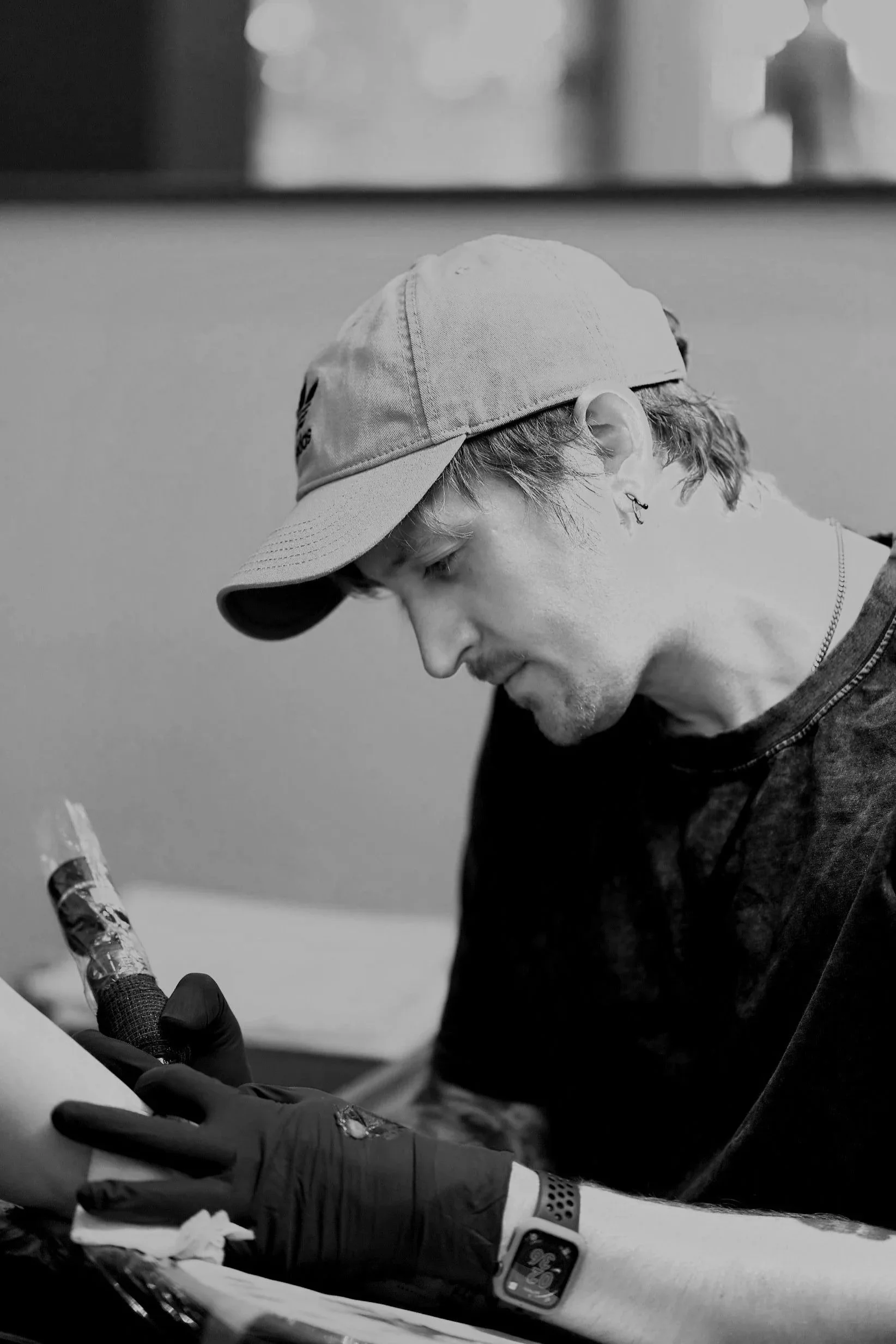 A man with a cap and earrings getting tattooed on his arm by a tattoo artist in a black and white photo. Tattoo artist Scranton Pennsylvania. Realistic tattoo artist Pennsylvania. NYC Microrealism. Fine Line Tattoo Scranton PA.