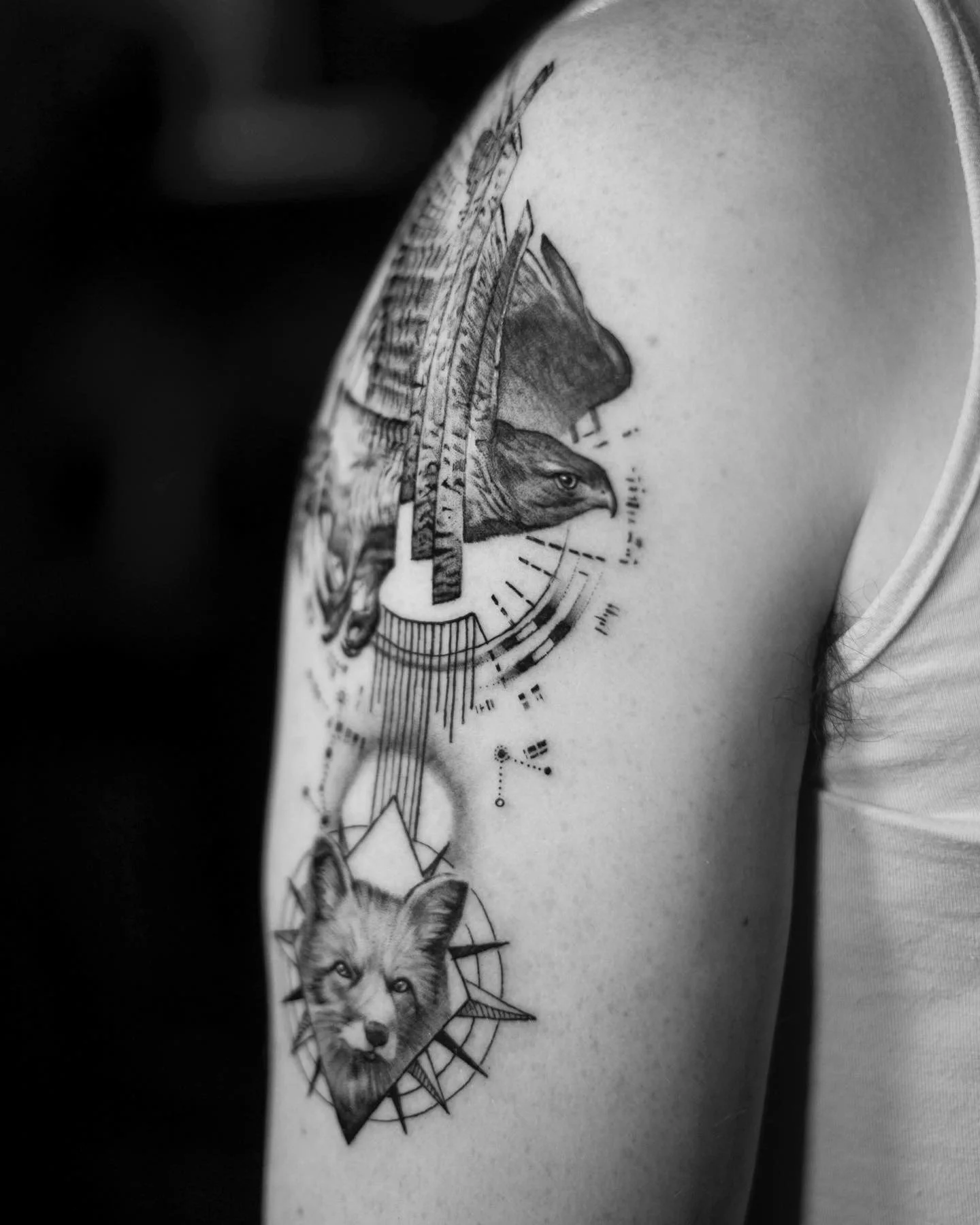 Black and white tattoo of an eagle and a wolf on a person's upper arm.