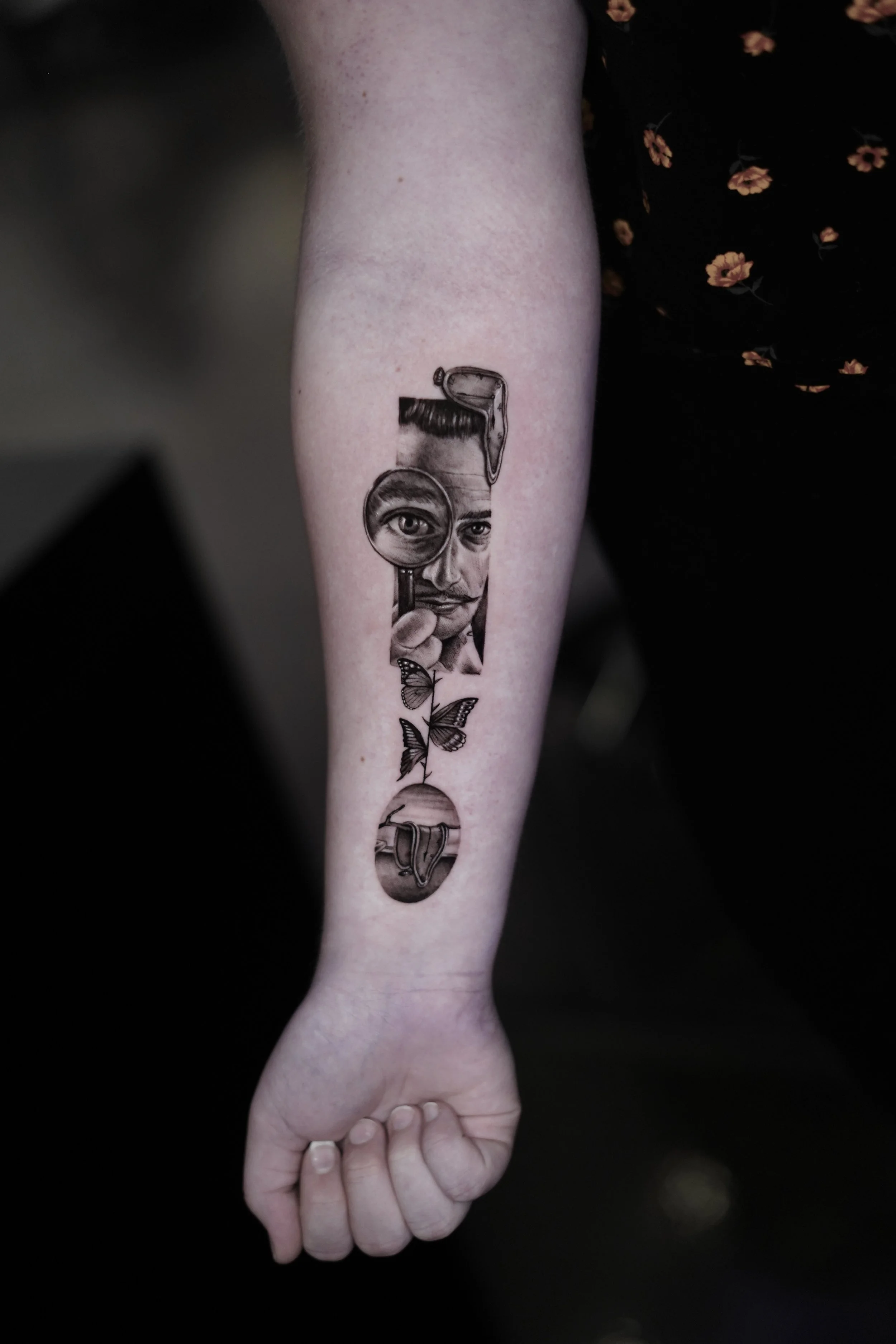 Tattoo of a person's face with a magnifying glass, a butterfly, and a planet with a ring on a person's forearm.