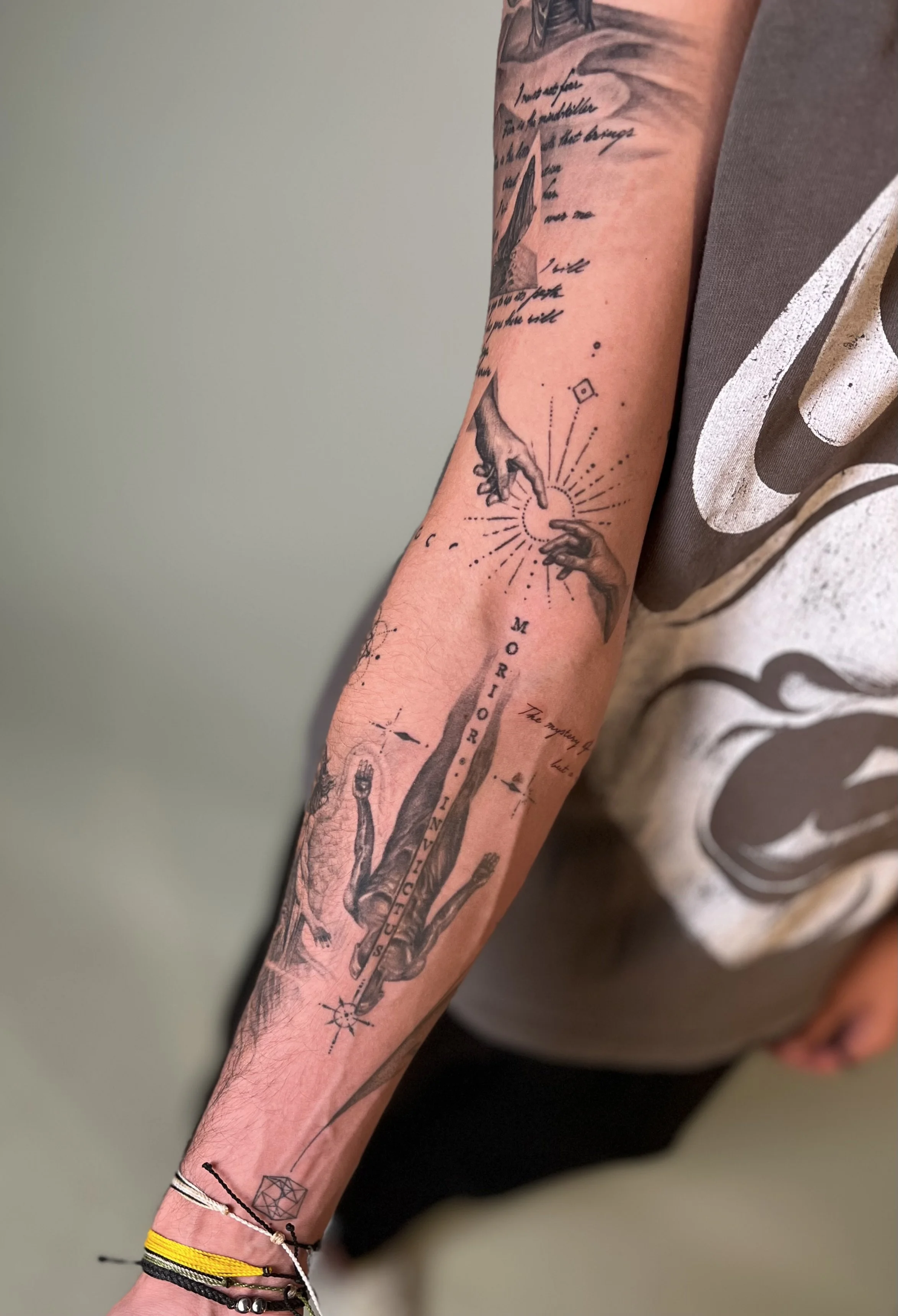 Tattoo of hands reaching towards each other with rays emanating from the point of contact, along with figures and text on the arm.