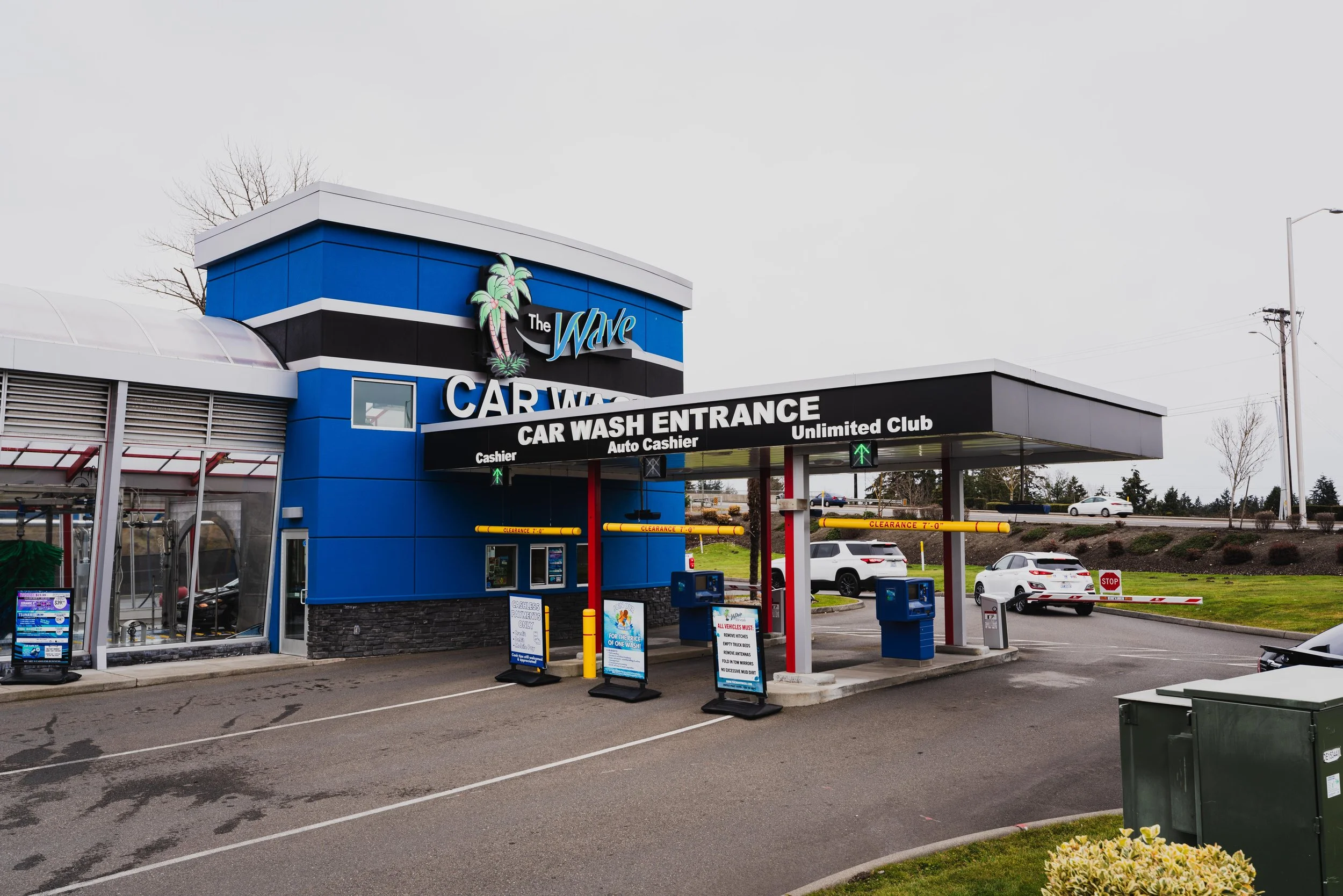 Exterior view of a car wash facility called The Wave with a blue and black building, car wash entrance, and parking lot with cars in the south sound.