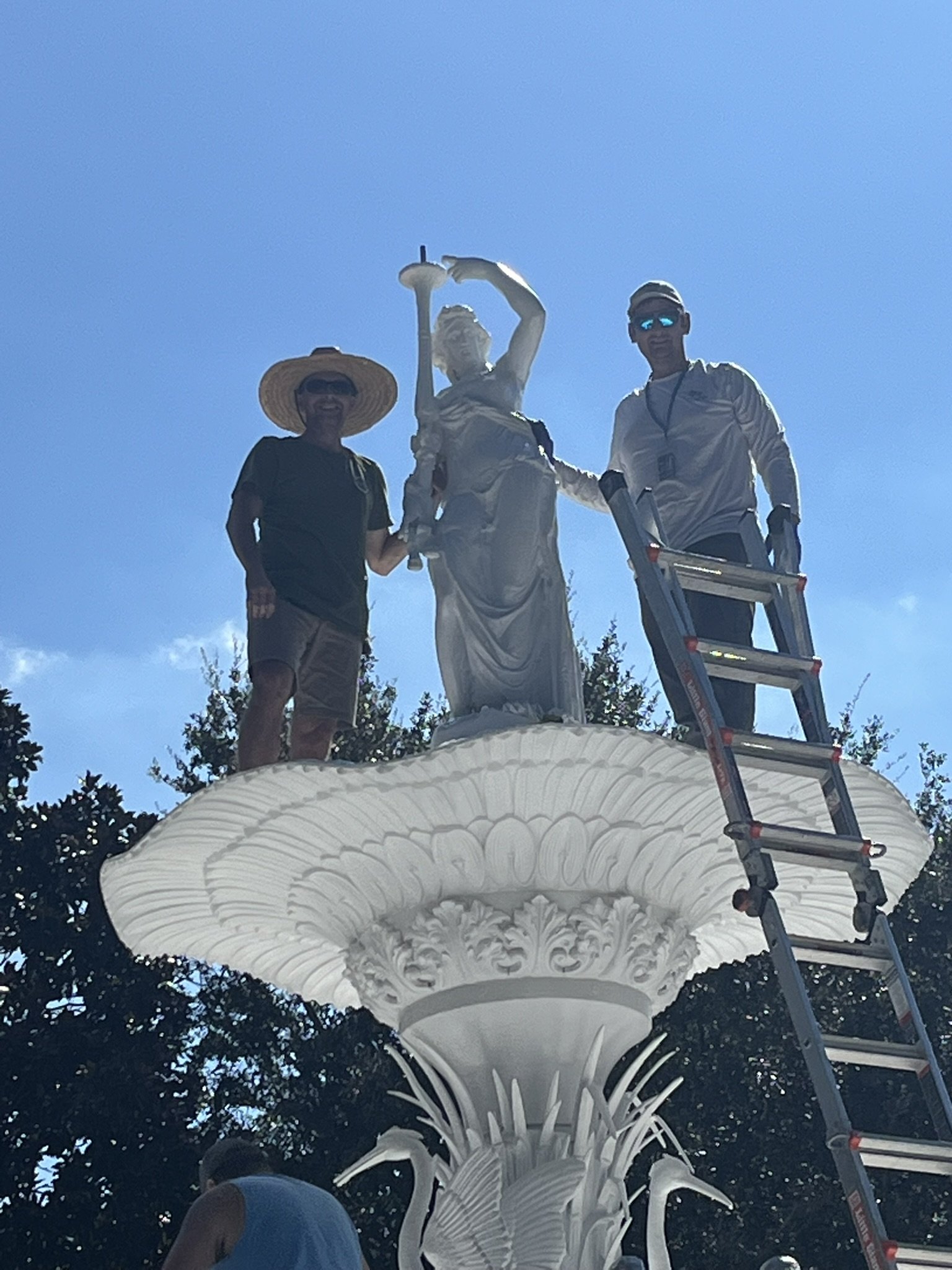 Three people standing around a large decorative white tree sculpture outdoors with a clear blue sky.