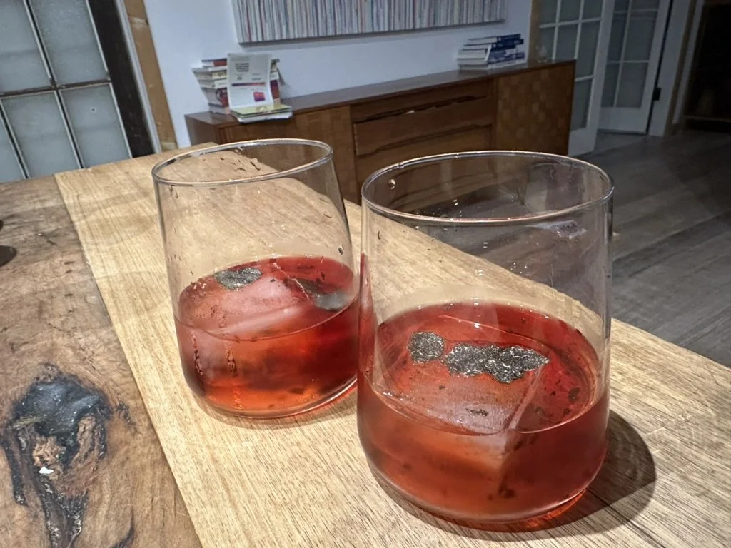 Two Truffle Negroni's with ice cubes on a wooden table in a cozy, well-lit room.
