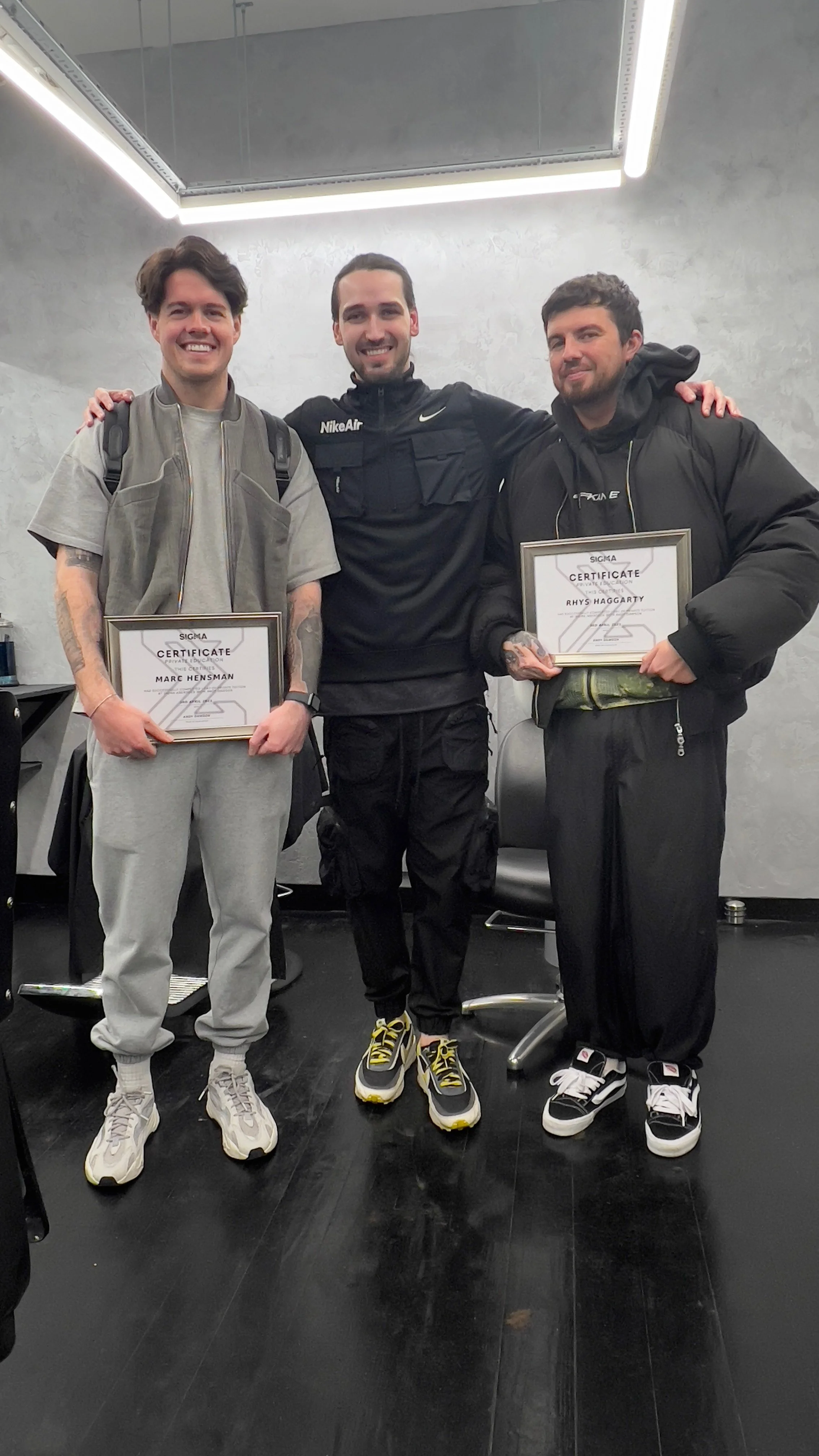 Three young men standing together indoors, holding certificates, smiling at the camera.