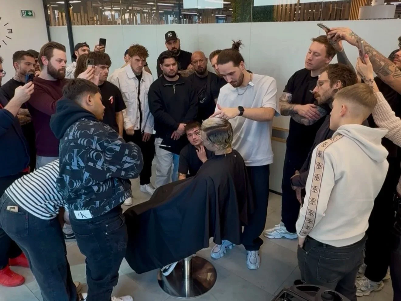 A group of people gathered around a hairstylist giving a haircut in a salon.