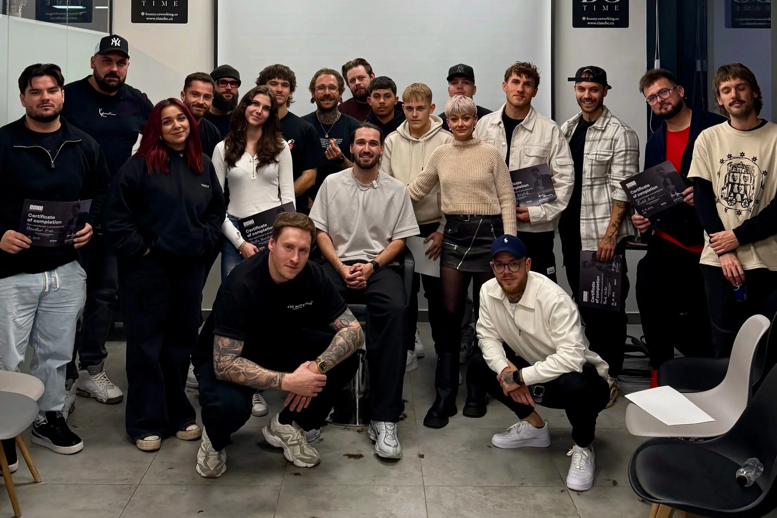Group of young adults and instructors celebrating at a graduation or completion event in a classroom or training room, some holding certificates.