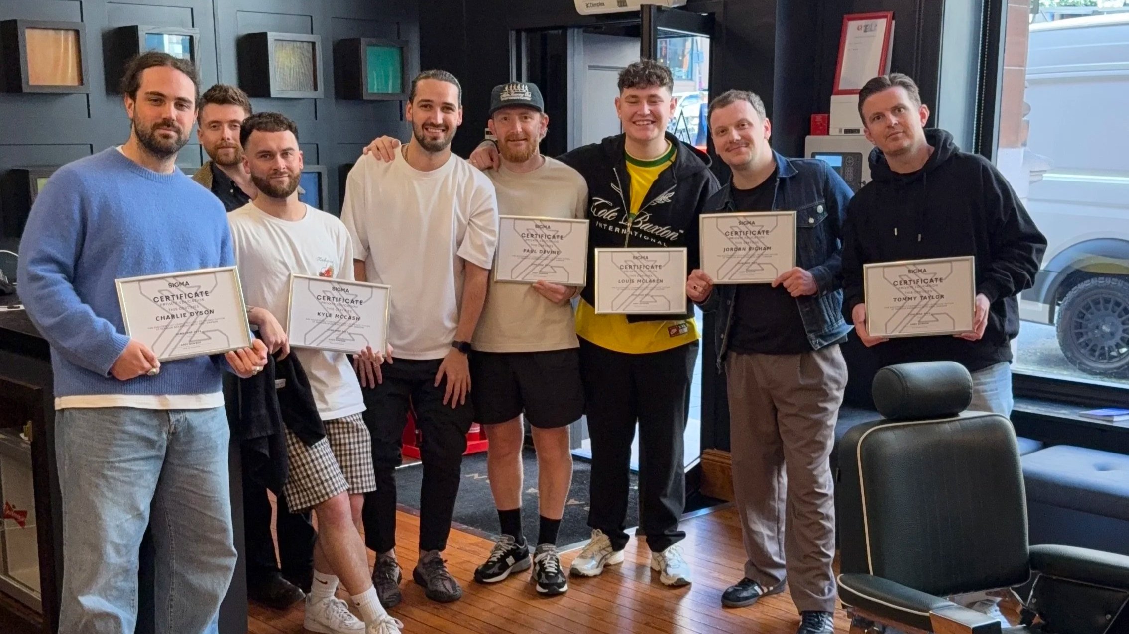 A group of eight men standing indoors, holding certificates, smiling for the photo.