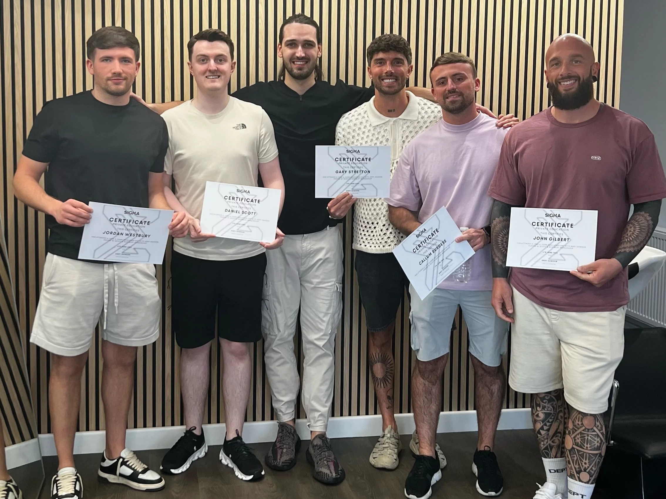 Six young men standing in front of a wooden wall, holding certificates of completion, smiling, and posing for a group photo.