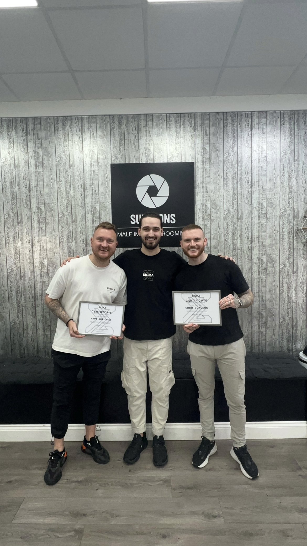 Three men smiling, holding certificates, standing in front of a sign that reads 'Syracons Male Intern Room.'