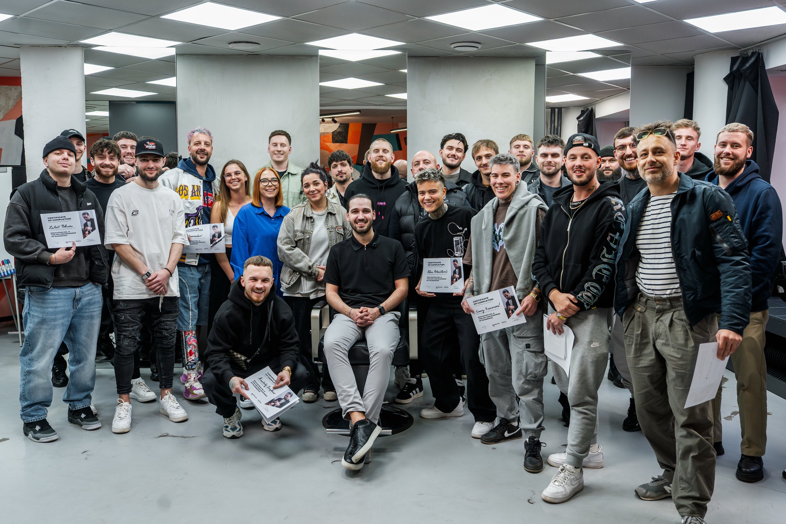 A large group of diverse young adults posing indoors for a photo, some holding certificates, smiling at the camera.