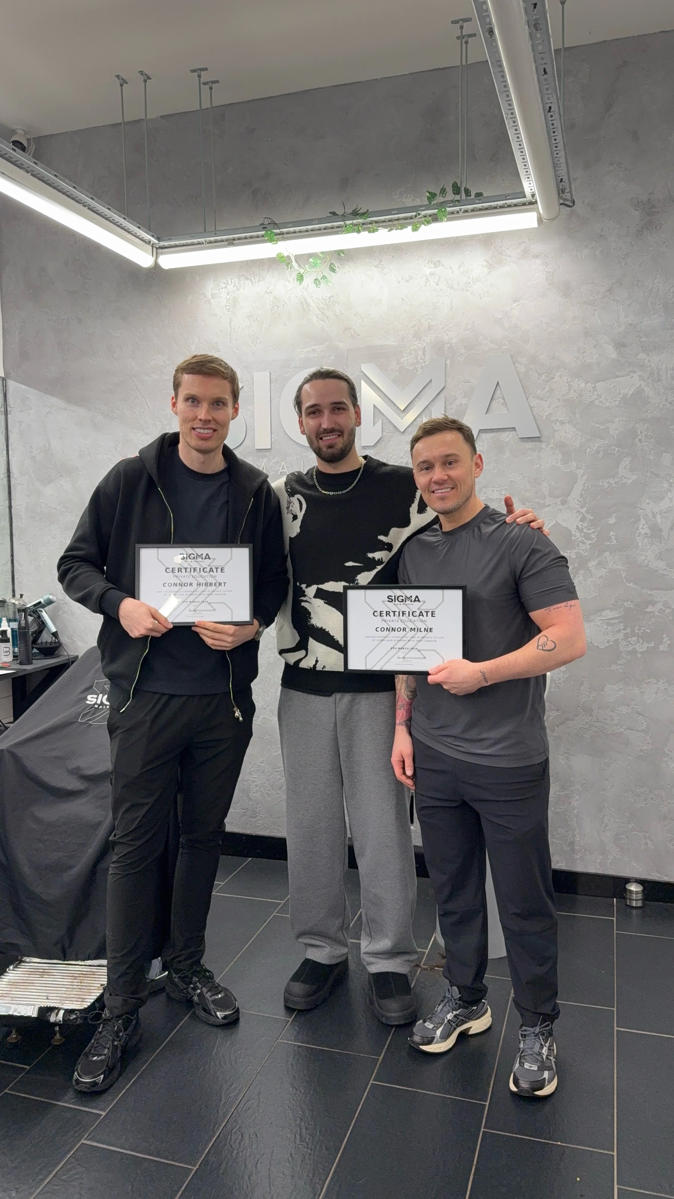 Three men standing in a modern office, two holding framed certificates, smiling, with Sigma logo on wall behind them.
