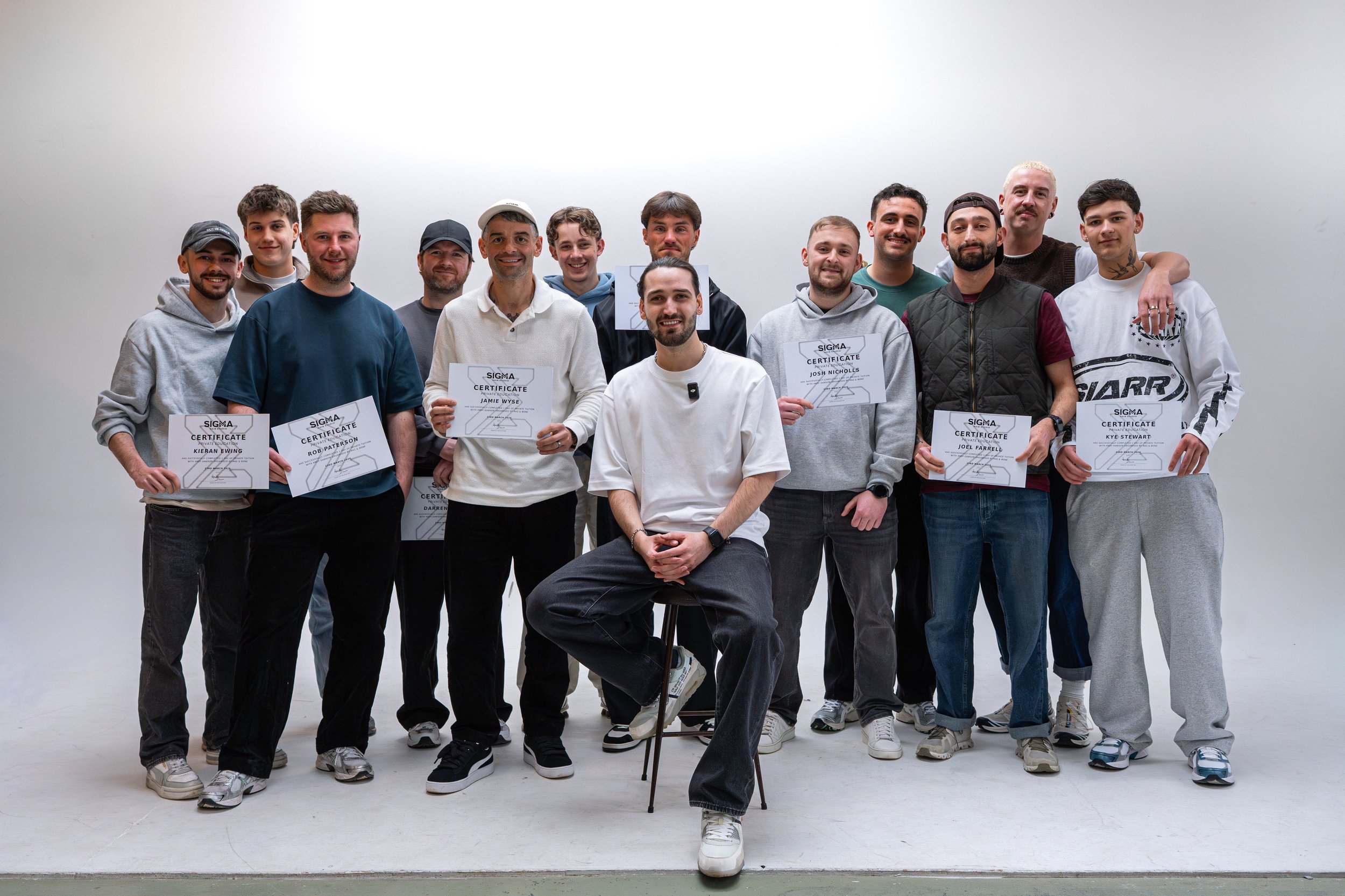 Group of young men standing together, holding certificates, in a photo studio with a white background.