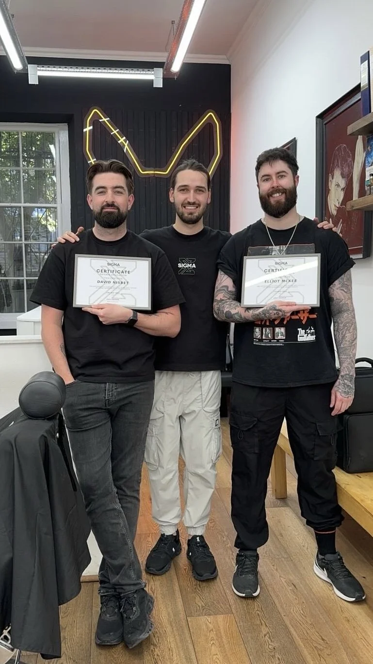 Three men standing together indoors, holding certificates, with a neon animal ears sign in the background and a window on the left side.