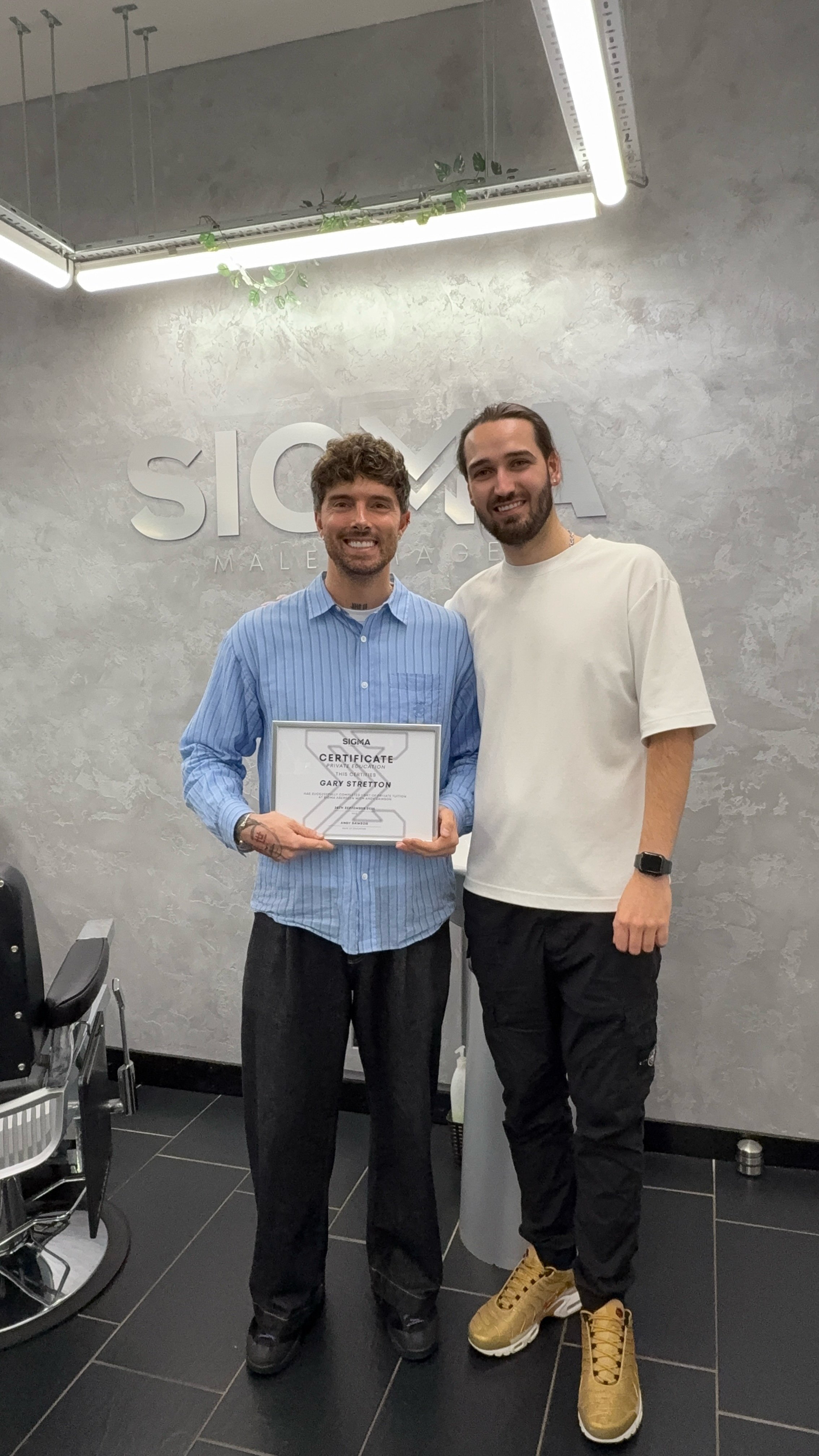 Two men smiling in a modern office, one holding a certificate, with the Sigma logo in the background.