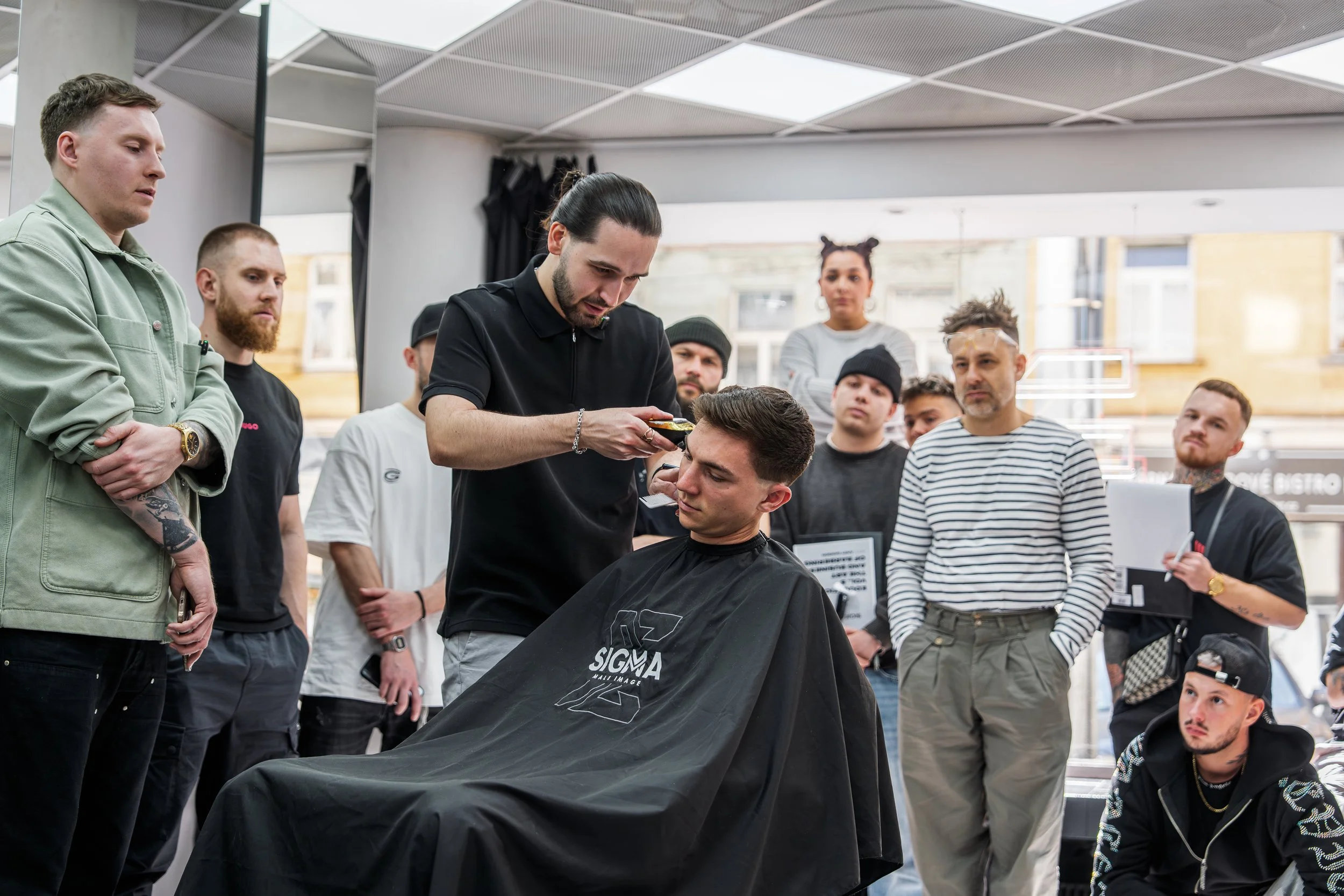 A group of men watching a barber give a haircut at a barbershop.