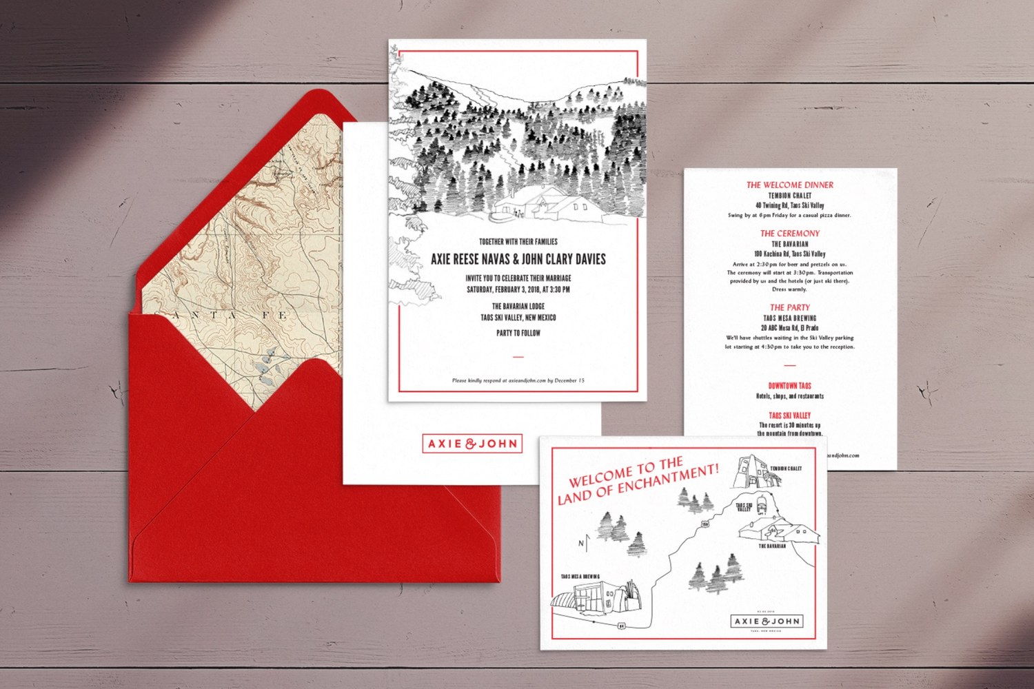 Wedding invitations and a map in a red envelope on a wooden surface. The invitations feature illustrations of mountain landscapes and scenic locations.