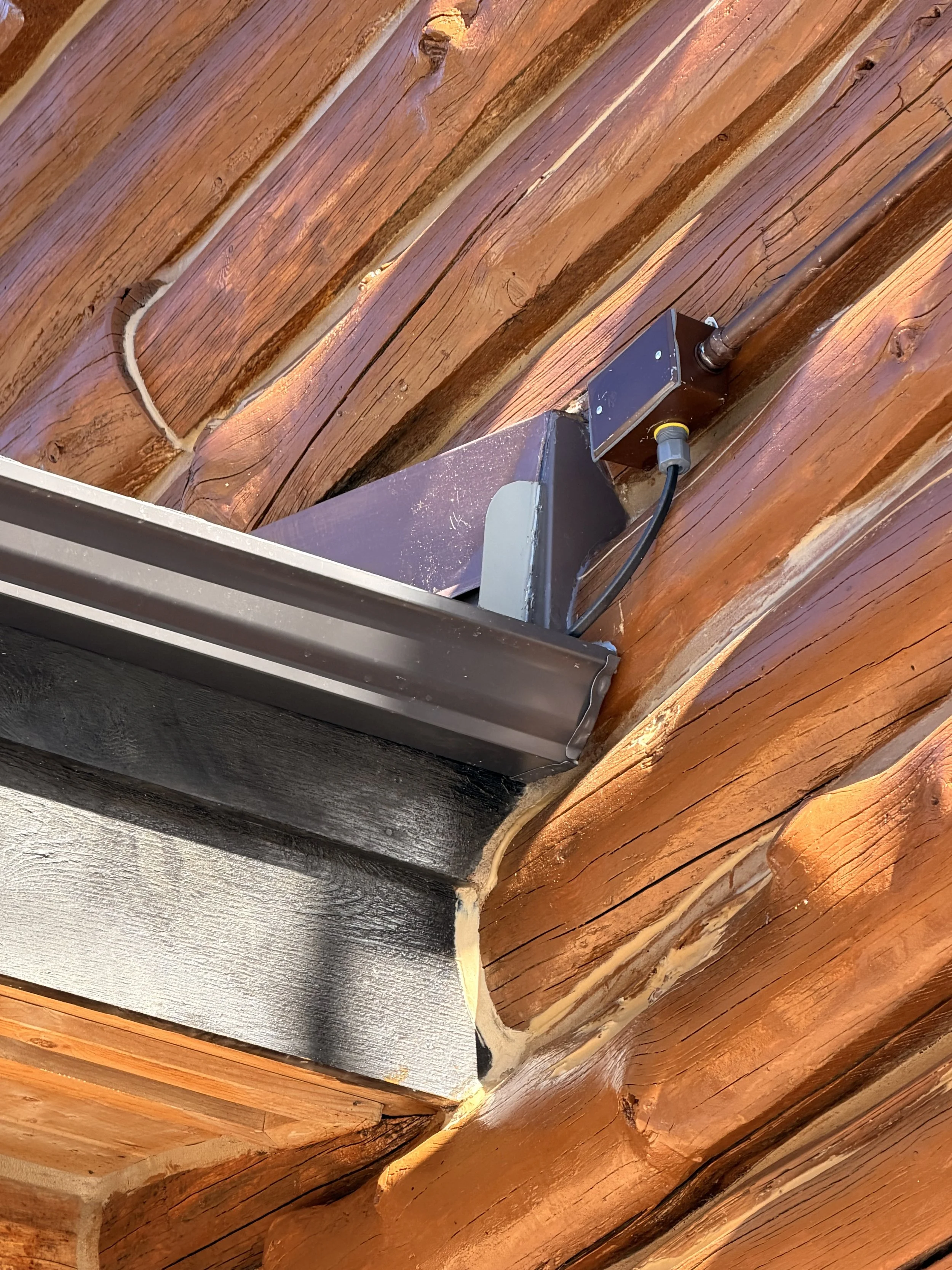 Wooden ceiling with exposed beams and electrical wiring in a metal electrical box.
