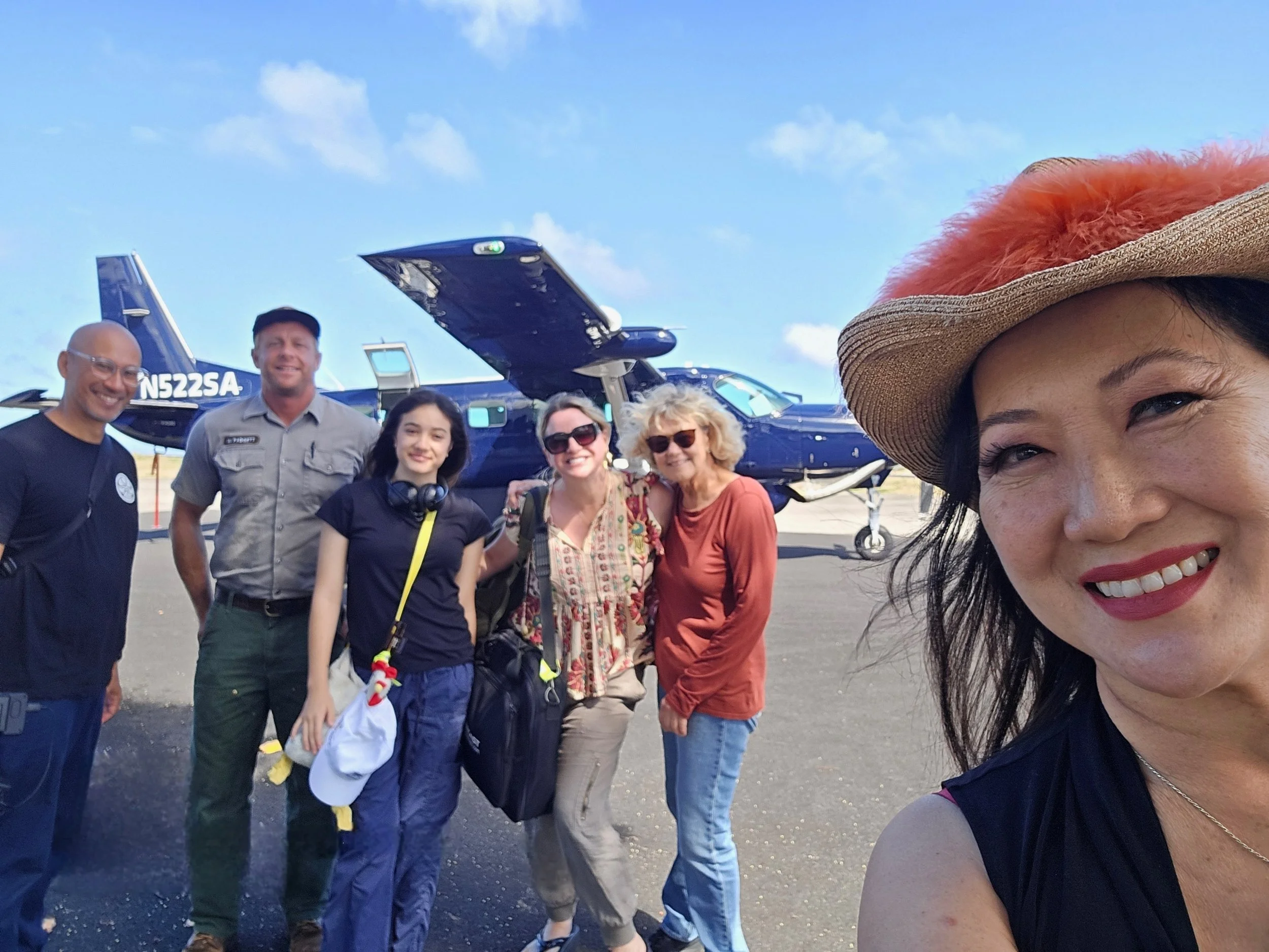 Six people on the tarmac of a small airport with a blue propeller plane behind them.