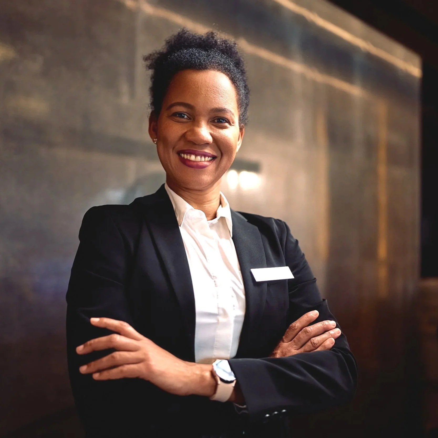 A confident woman in business attire, smiling with arms crossed in an office or professional setting