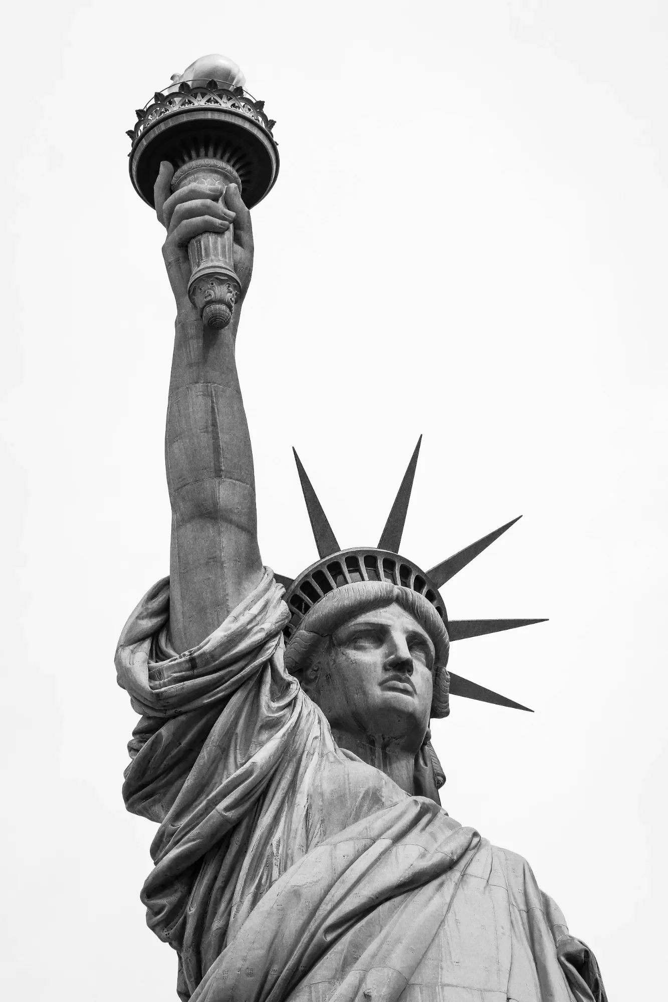 Close-up of the Statue of Liberty's face and upper hand holding a torch, in black and white.