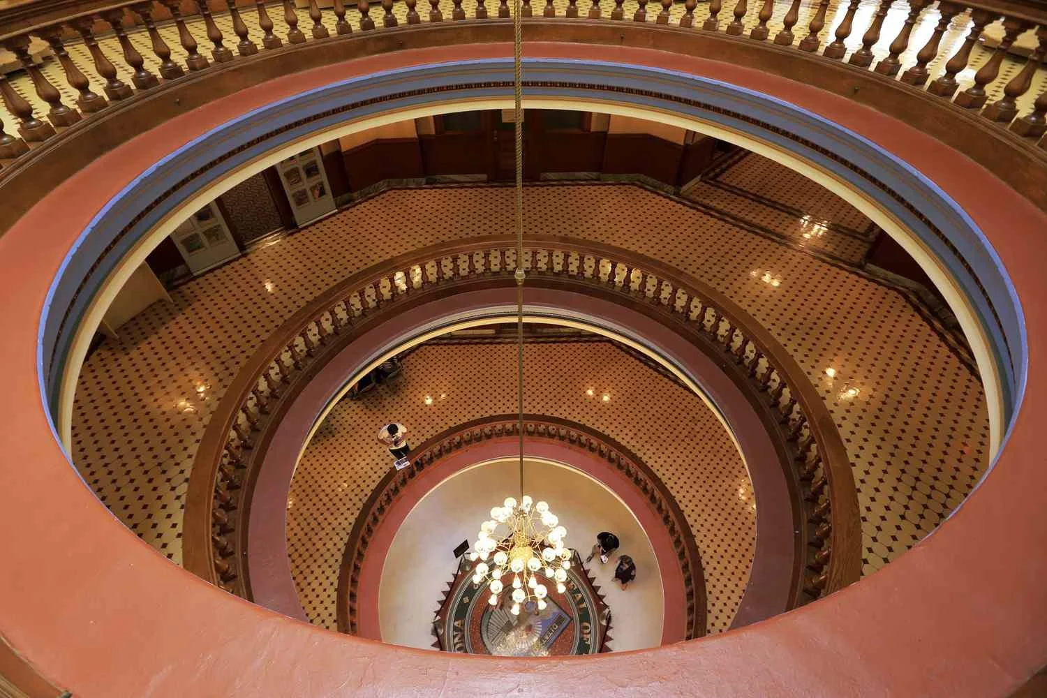 Interior view of a multi-story building with curved balconies and a central chandelier hanging from the ceiling, looking down from the top floor.