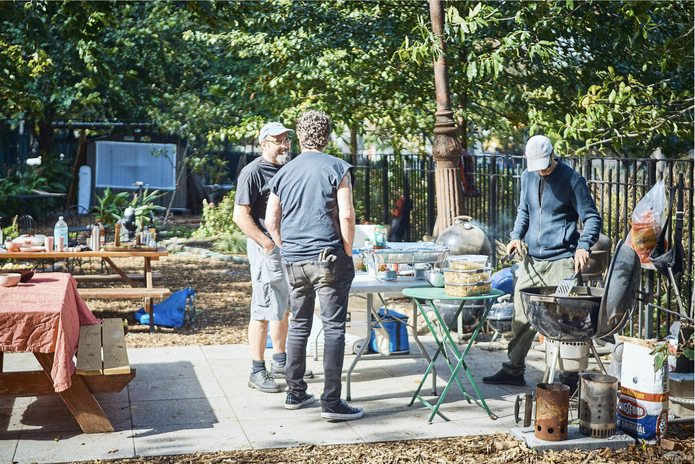 An outdoor community space with people grilling at barbecues.