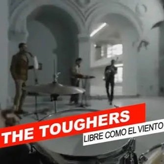 Three people walking through a spacious, arched hallway with white walls and a fountain in the foreground. Overlaid text reads 'THE TOUGHERS' and 'LIBRE COMO EL VIENTO'.