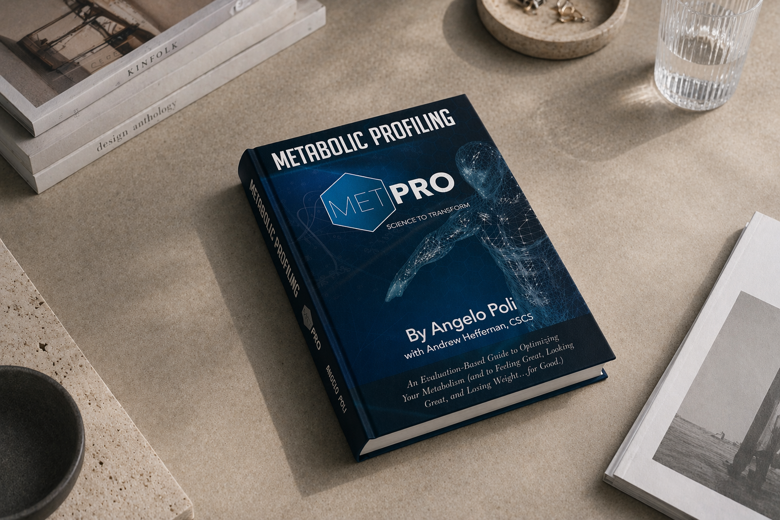 A book titled 'Metabolic Profiling METPRO' by Angelo Poli with Andrew Heffernan, CSCS, placed on a beige surface. The book cover features a digital illustration of a human figure with a network of lines and points. Other books, a glass of water, a small bowl, and a booklet are partially visible around it.