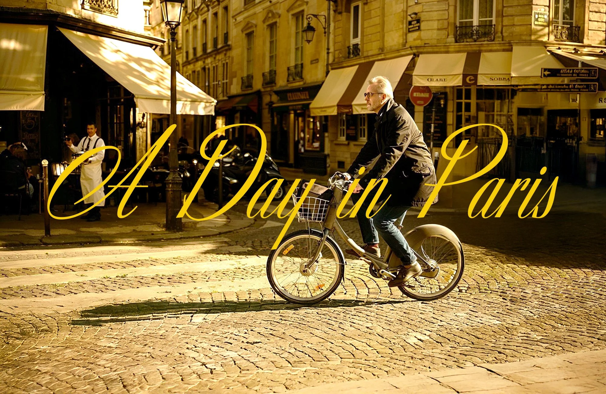 A man riding a bicycle on a cobblestone street in Paris during the daytime, with cafe terraces and yellow buildings in the background. The words 'A Day in Paris' are written across the image in yellow cursive text.