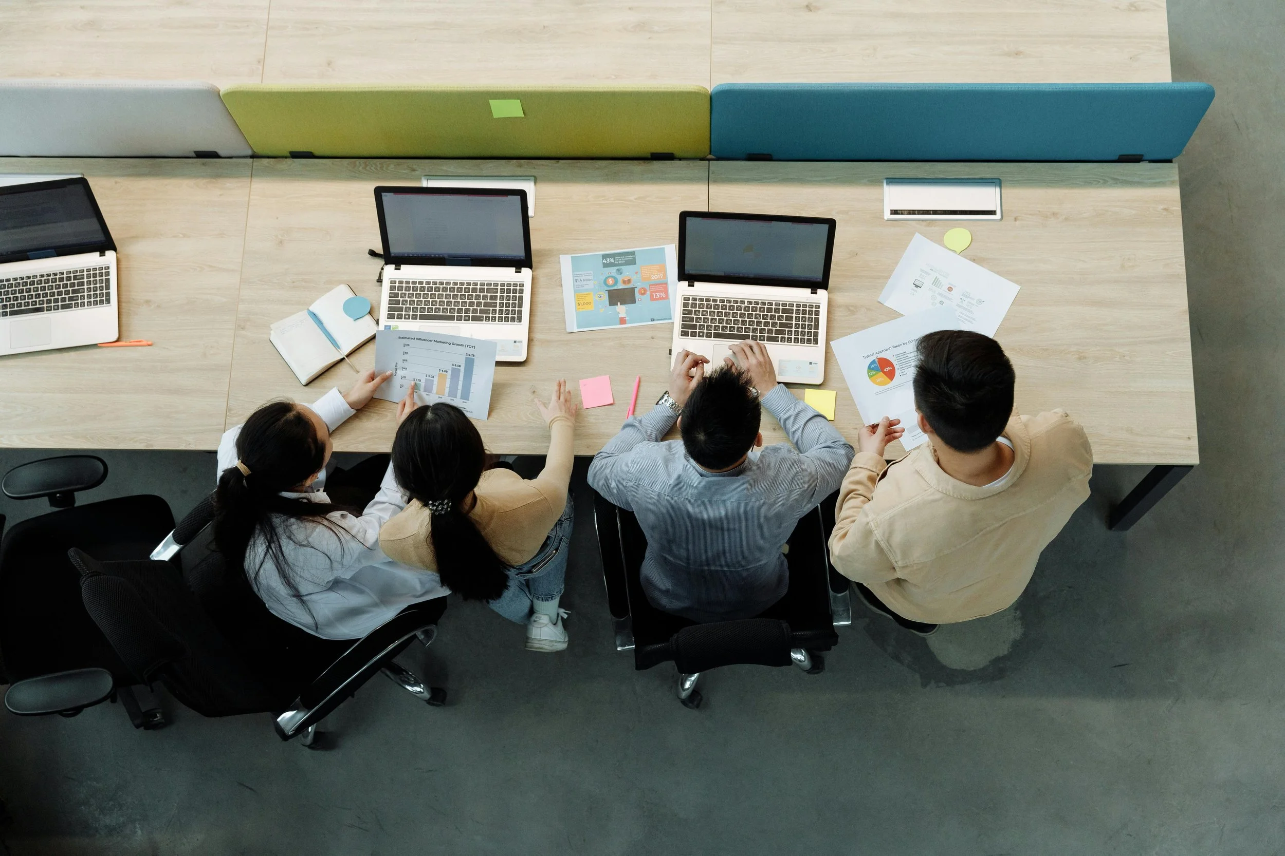 A group of people sitting around a long wooden table in a meeting room, working on laptops and reviewing housing data.