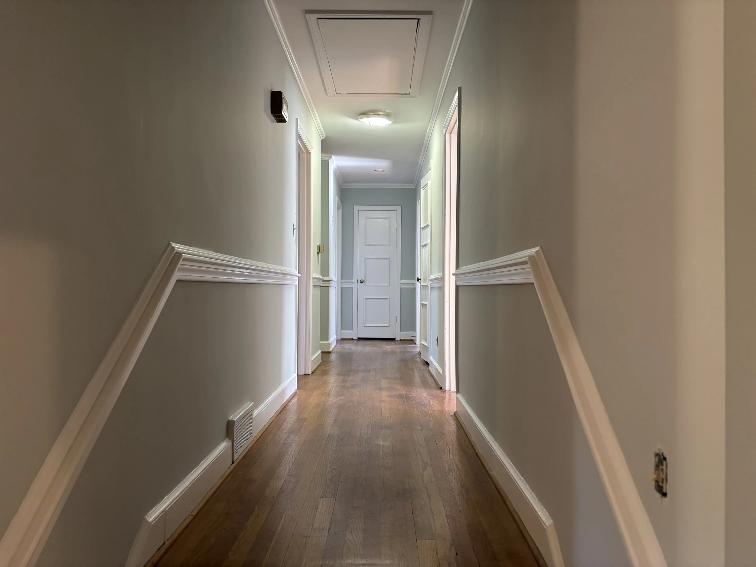 Empty hallway with beige walls, white trim, wood flooring, and closed white doors at the end.