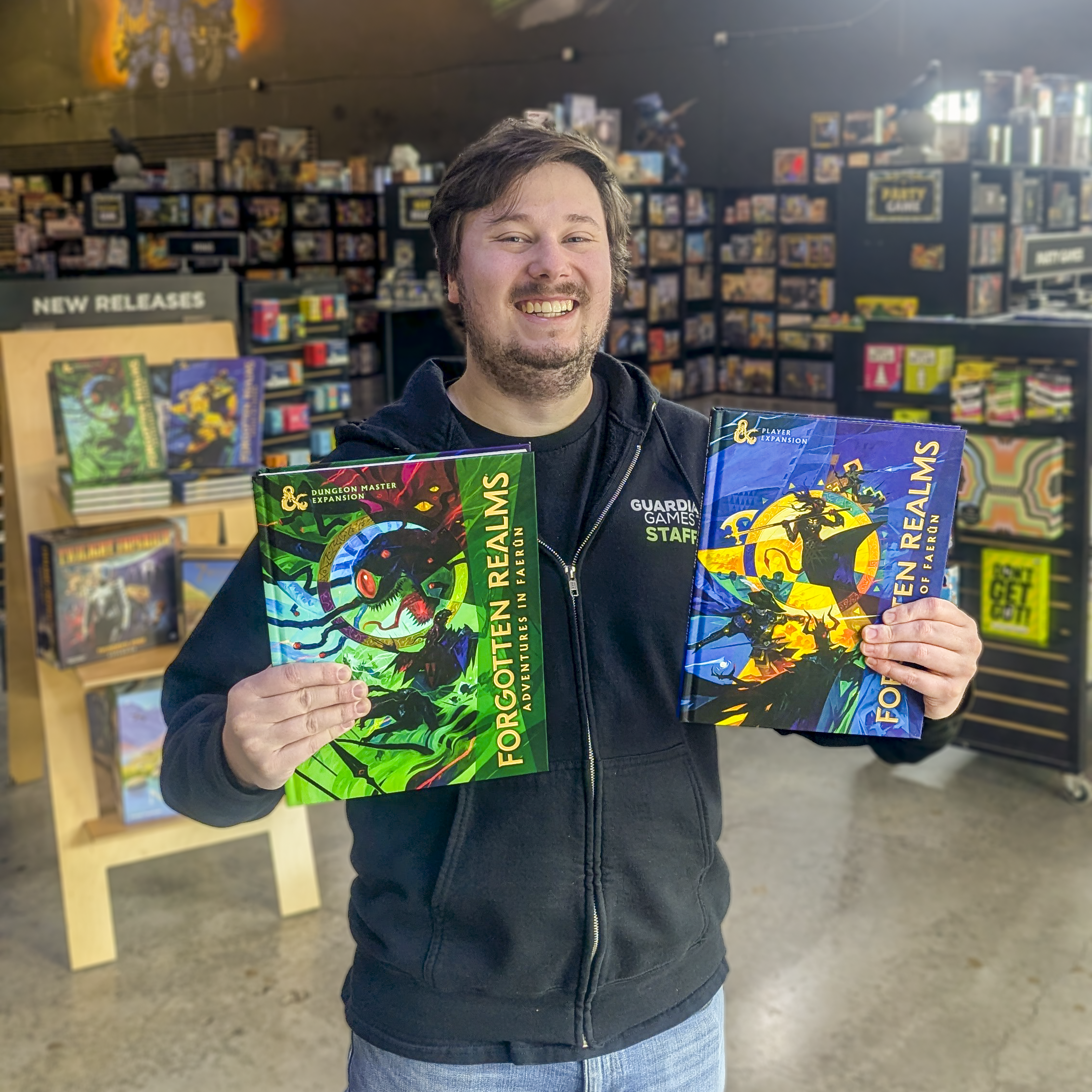 A smiling man holding several fantasy and role-playing game books inside a bookstore or game shop, with shelves of books and games in the background.