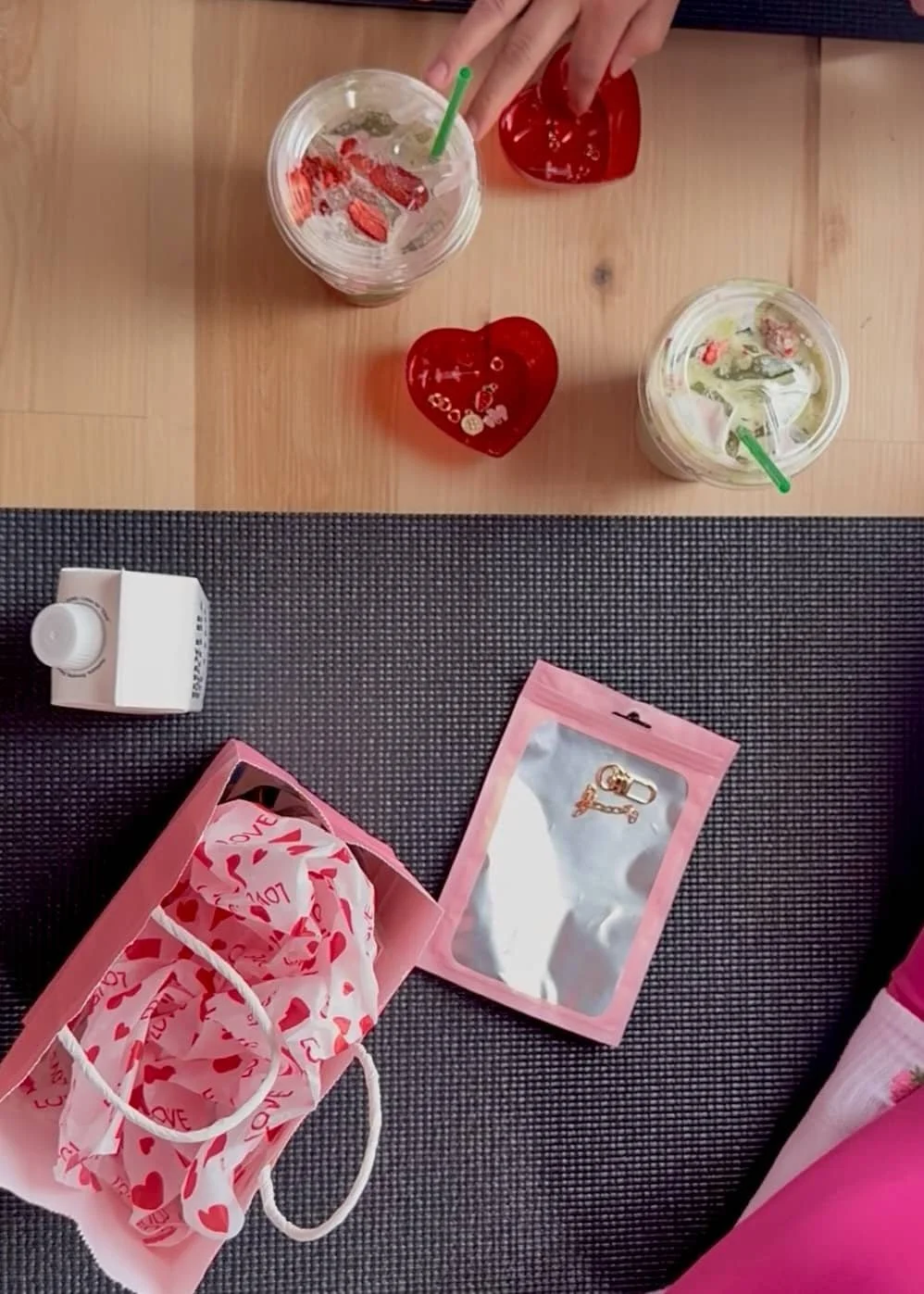 Two glasses of iced beverages with soothing colors and straws, red heart-shaped ornaments, a small perfume bottle, a pink gift bag with a tissue paper and 