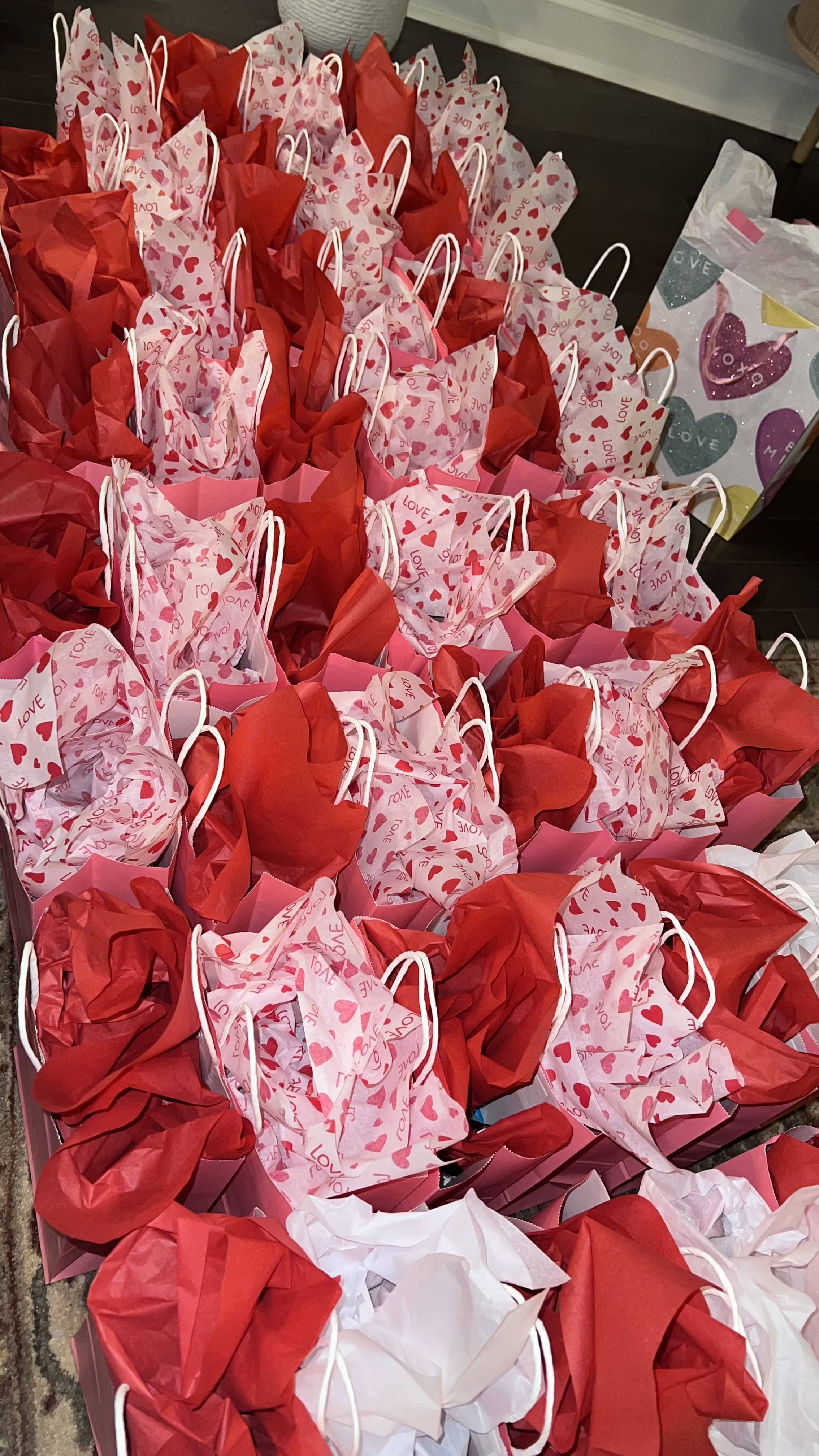 Multiple small gift bags in red, pink, and white with heart and love themed wrapping, arranged on a table, possibly for Valentine's Day or a romantic occasion.