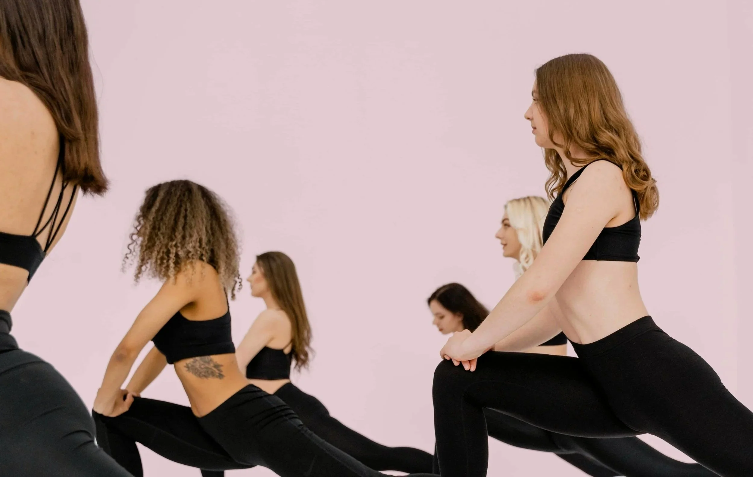 3 women wearing black activewear in a single file while doing the warrior stretch pose.