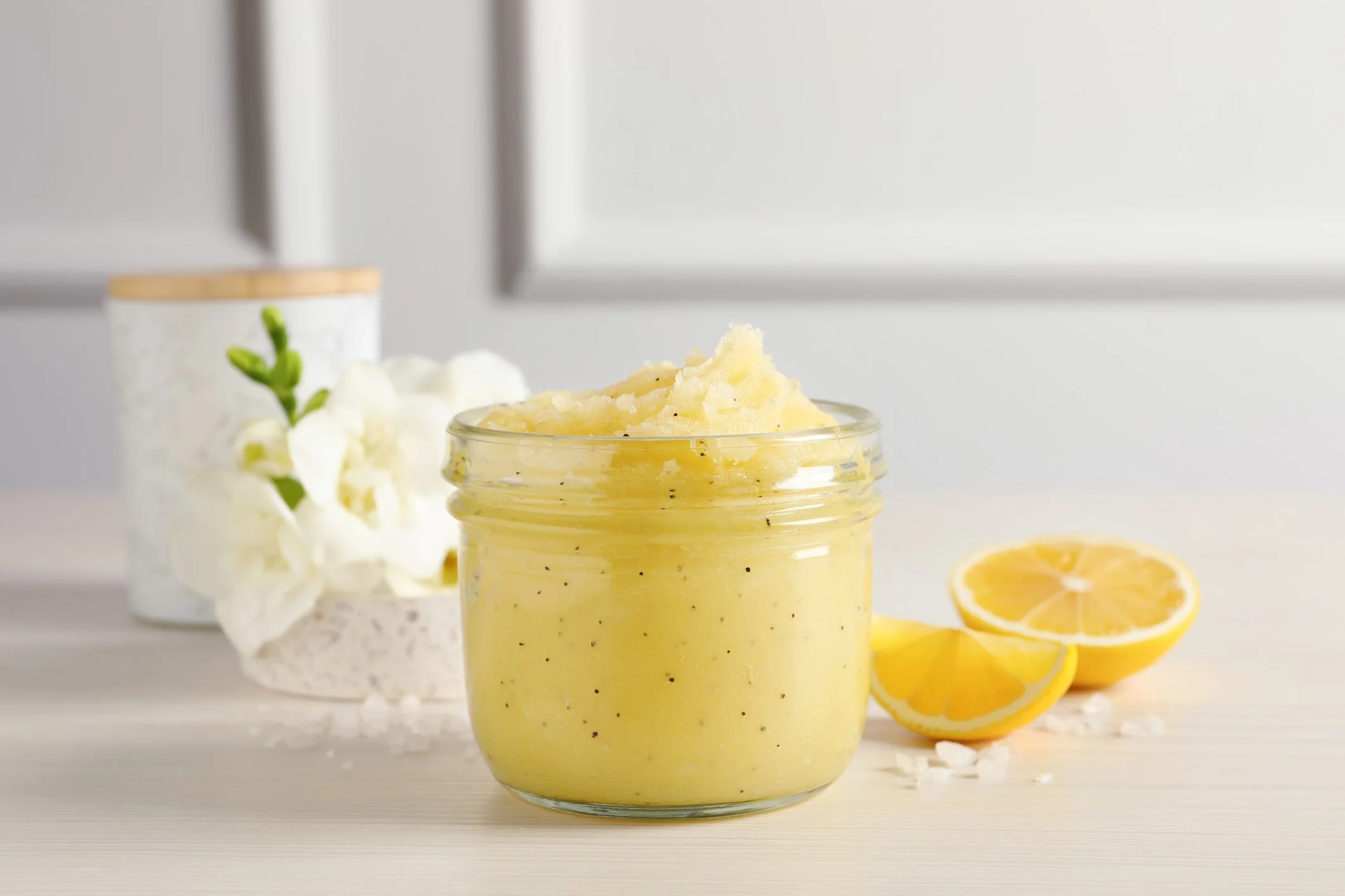 A jar of lemon scrub with a lemon slice and white flowers in the background.