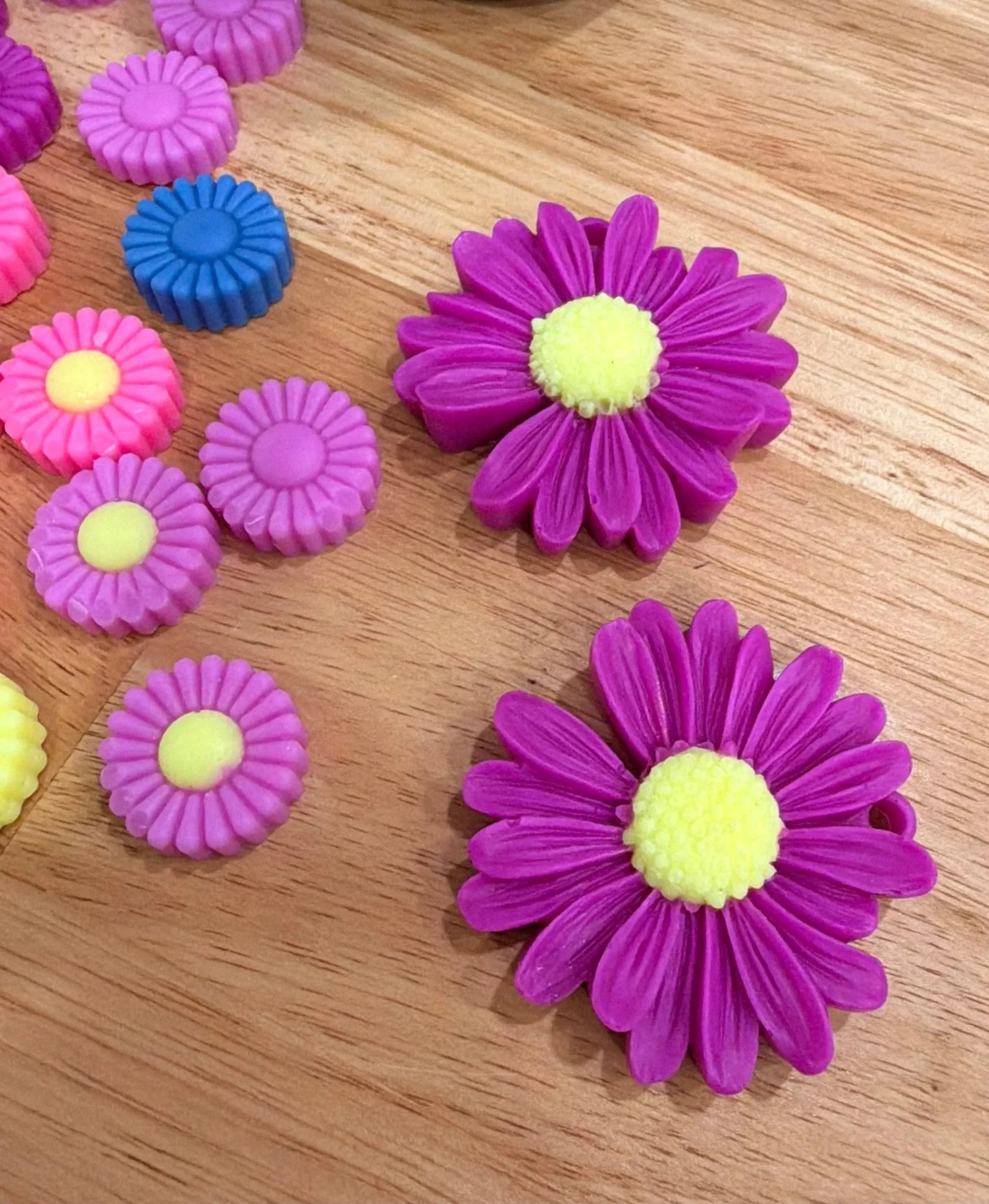 Colorful plastic flower and daisy-shaped beads arranged on a wooden surface.
