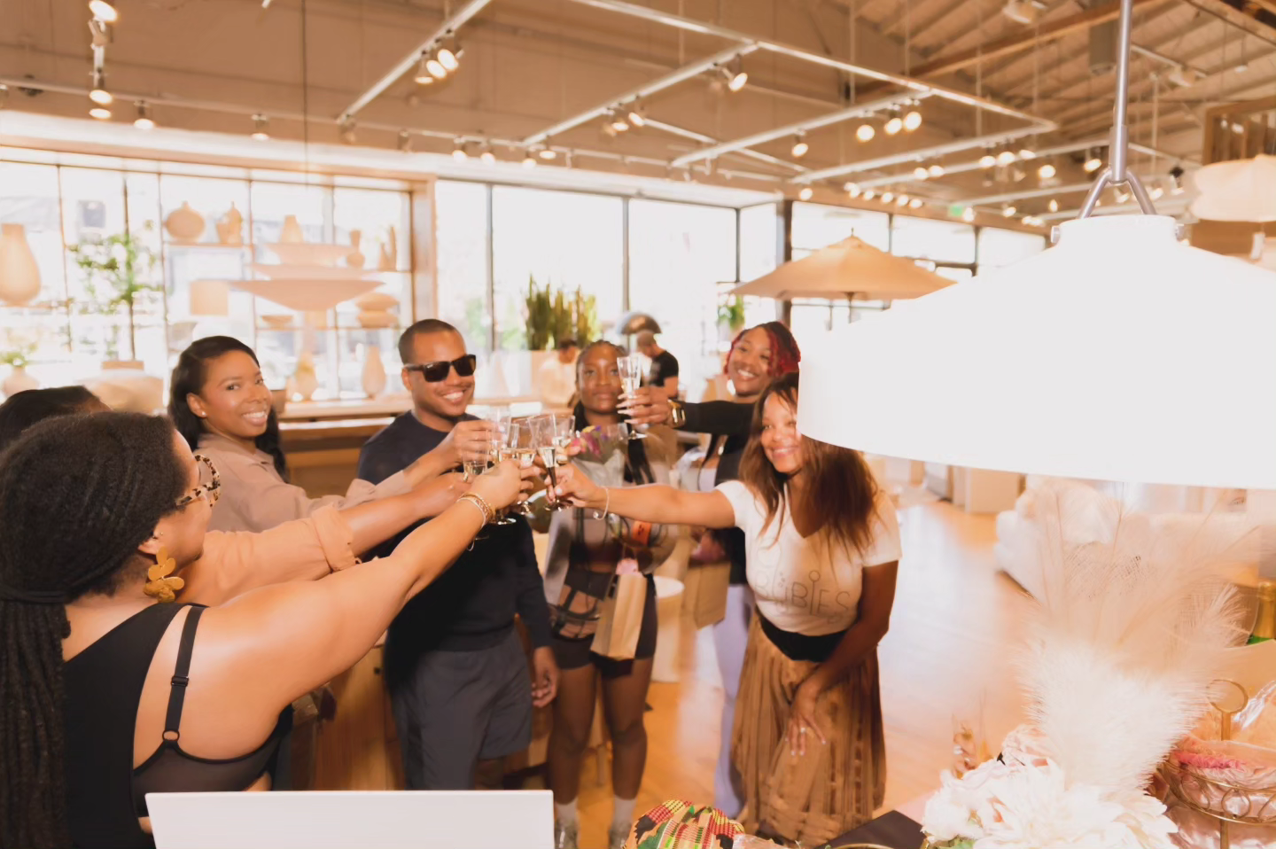 A group of friends celebrating with champagne at a restaurant or cafe, raising glasses for a toast, in a bright, modern setting.