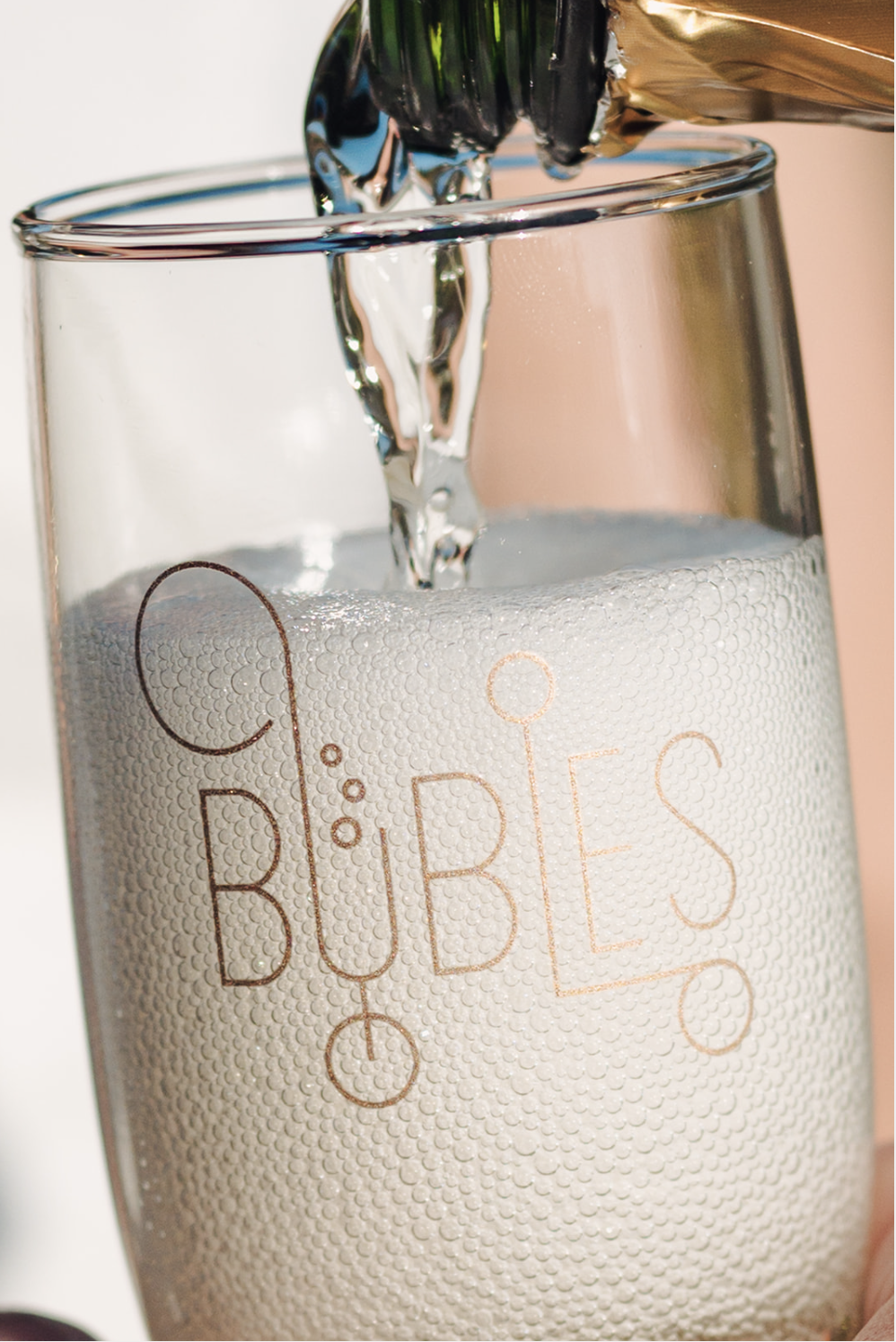 Sparkling water being poured into a glass with the word "BUBBLES" written on it, accompanied by a bubble design.