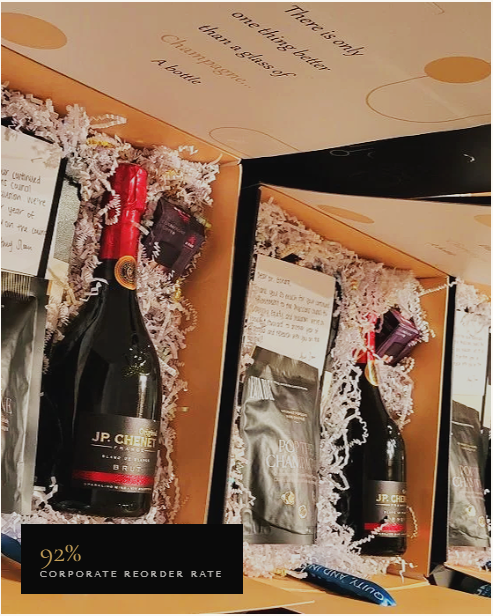 Decorative Christmas display with bottles of JP. Chenet champagne, wrapped in glittery pink and silver paper, surrounded by white tinsel, with a holiday card and slogan in the background.