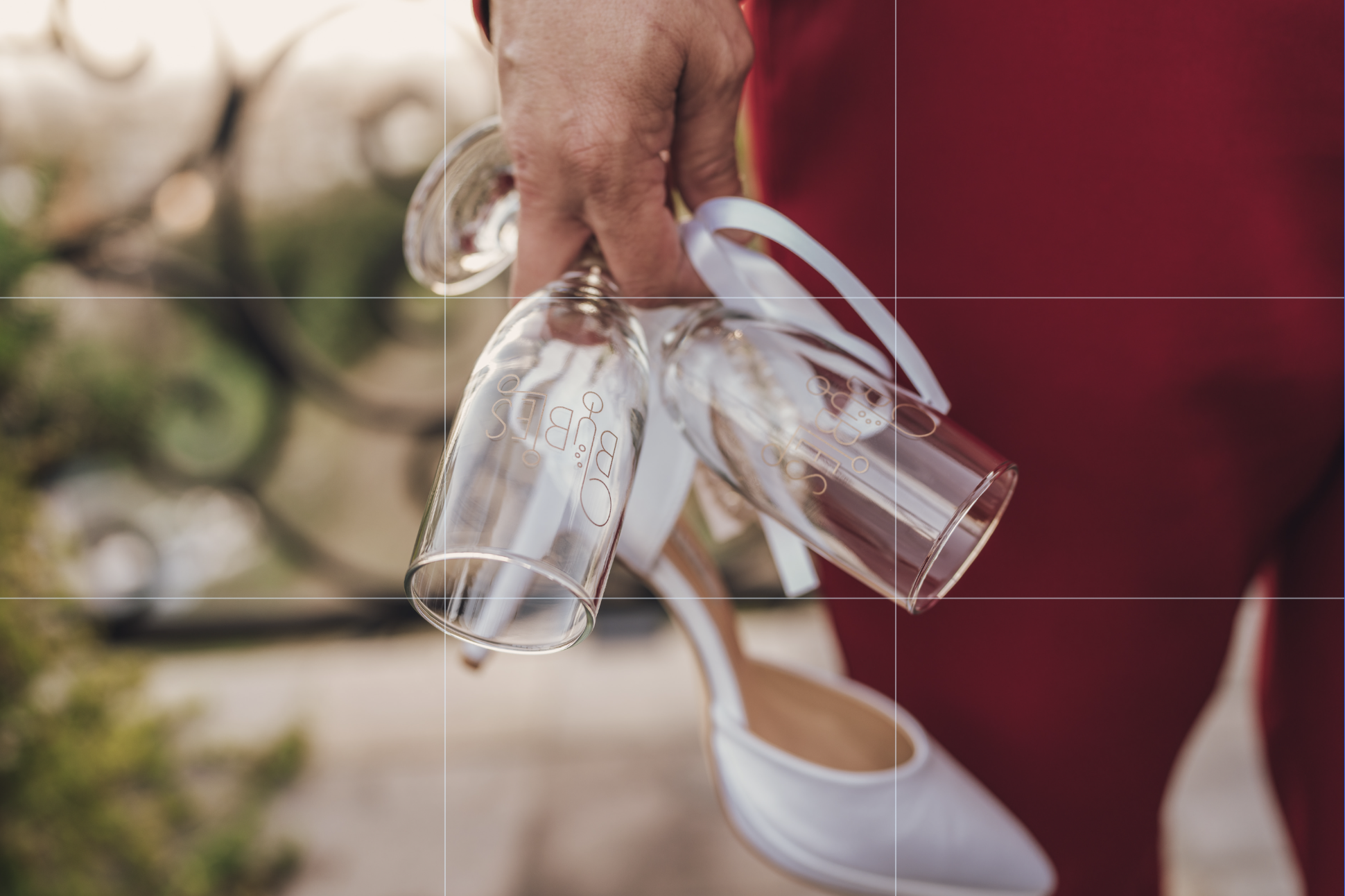 Person holding a few empty glasses with white ribbons tied around them, standing outdoors.